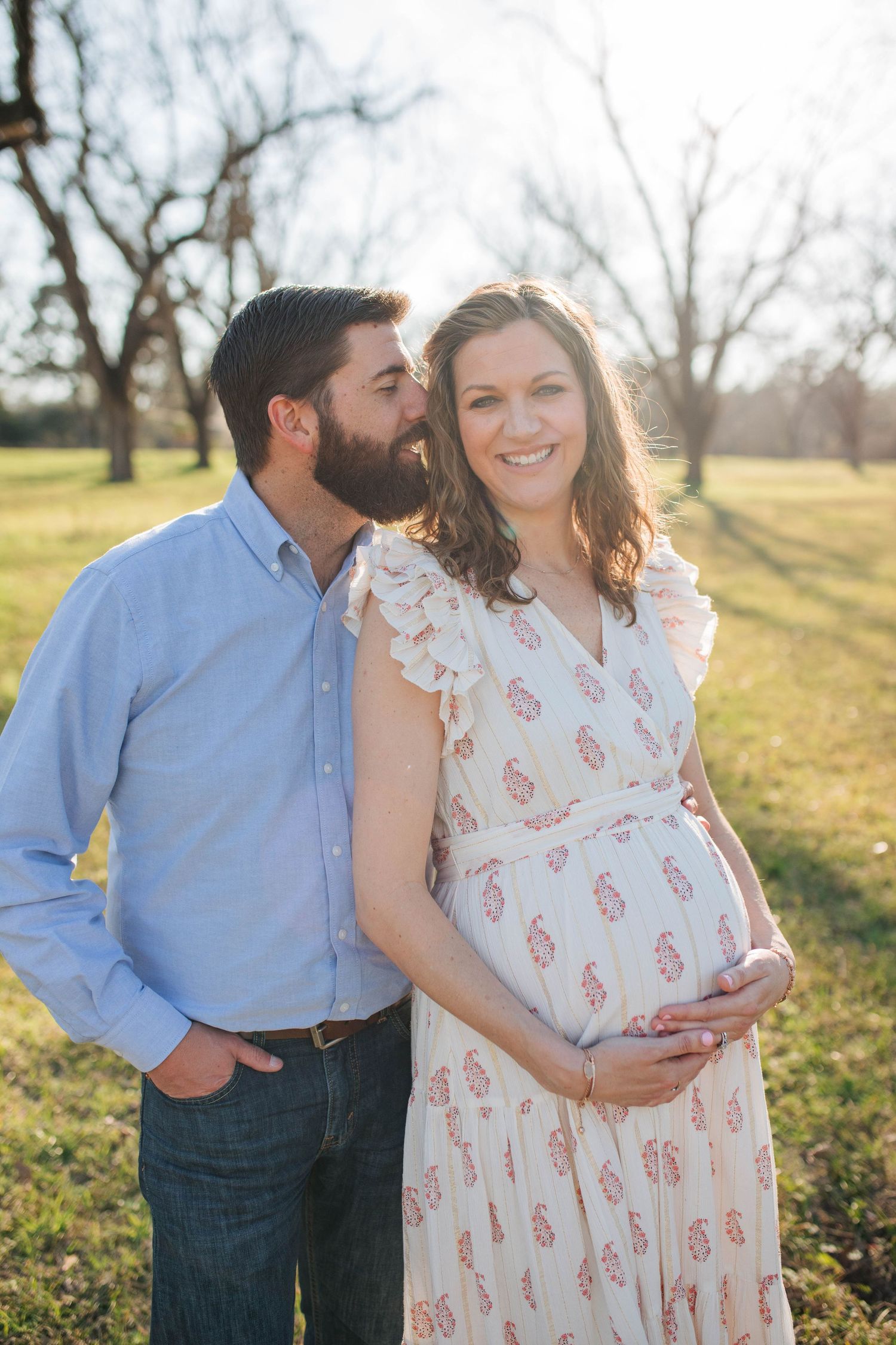 Couple embracing in outdoor maternity photo session during golden hour.