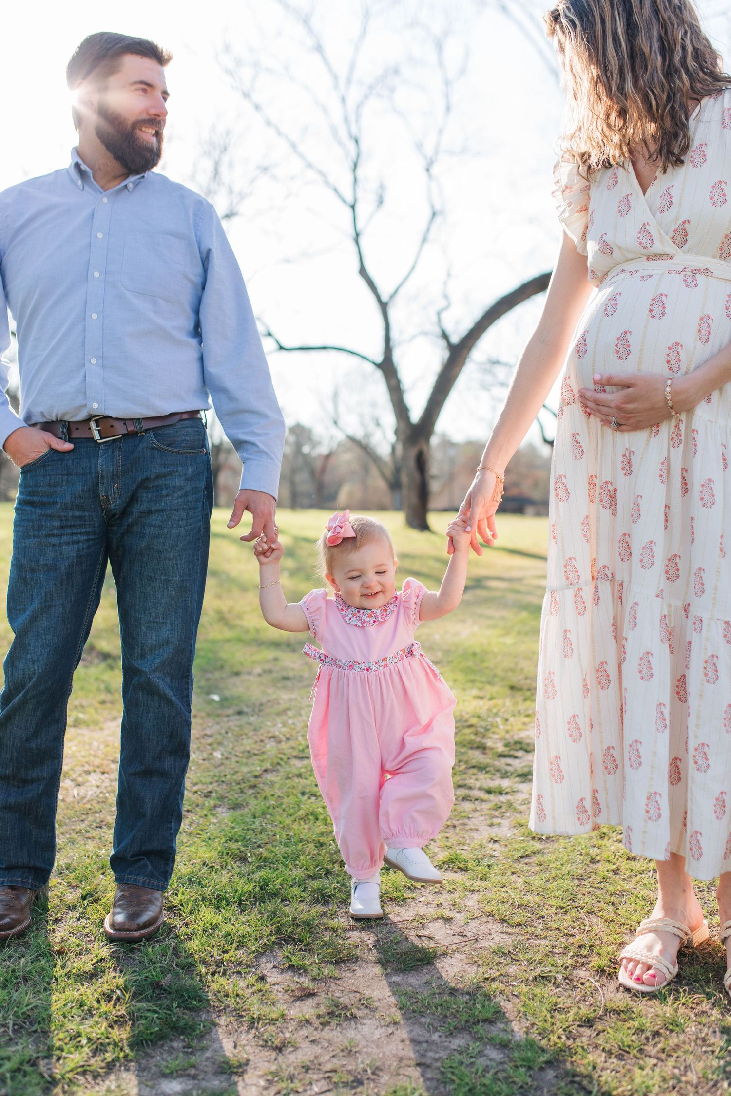 Family walking together outdoors with small child in pink dress.