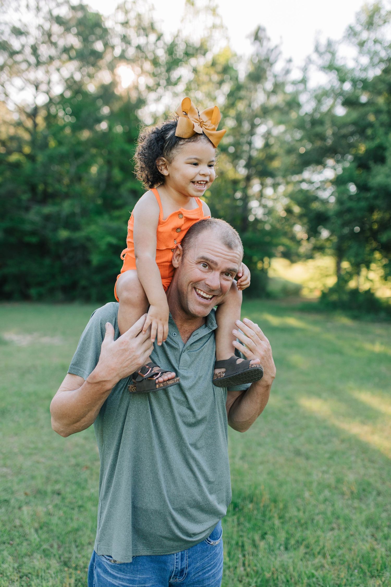 A joyful outdoor moment as a child rides on shoulders in a green field at sunset.