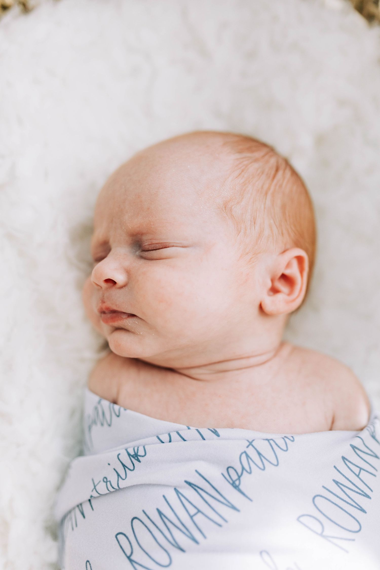 Peaceful sleeping newborn in patterned swaddle against white textured background.