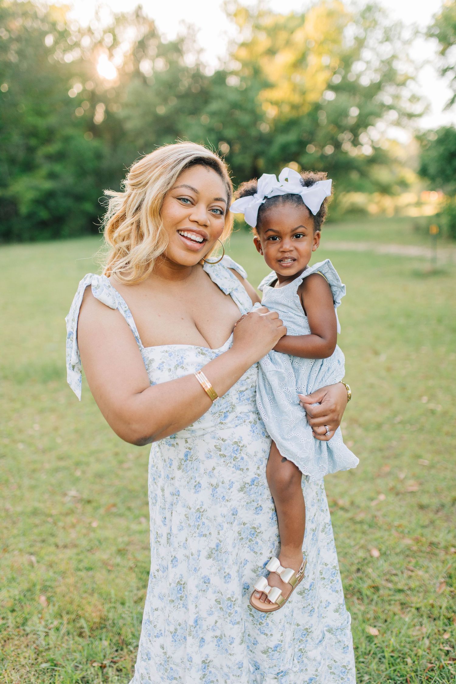 A mother and child wearing matching floral dresses share joyful moments in a sunny outdoor setting.