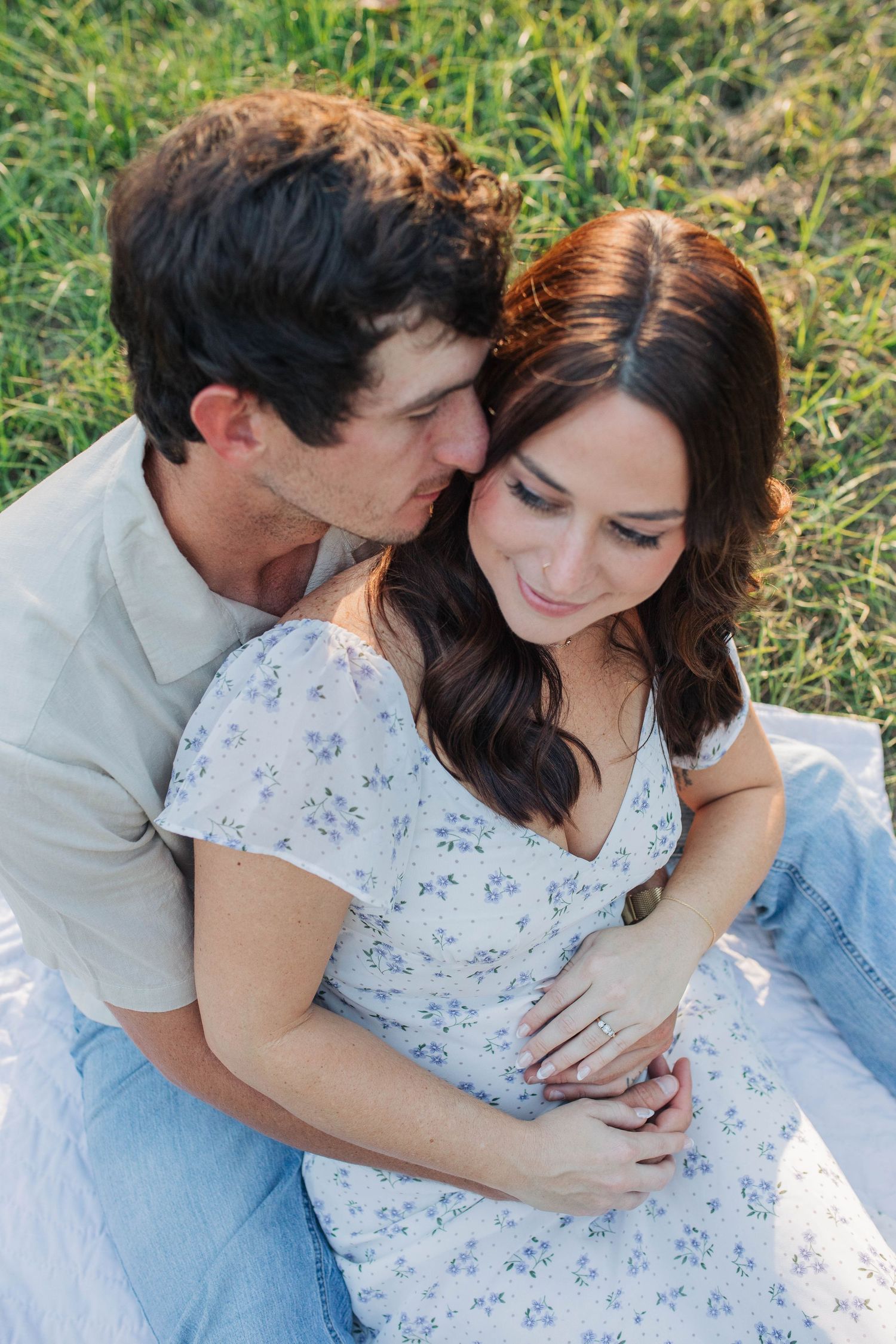 Tender embrace between couple on blanket in grassy field.
