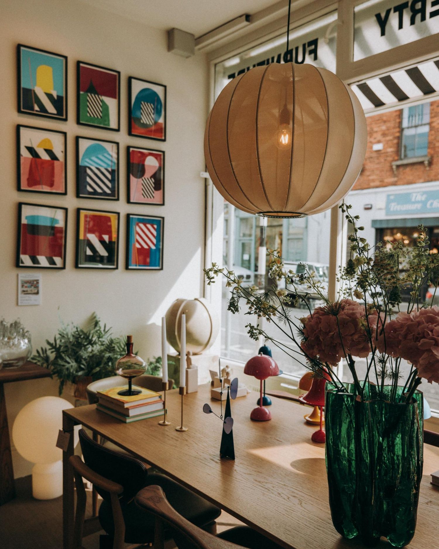 Nordic interior with a wooden dining table, pink flowers in a green vase, colourful modern art on the wall, and a large fabric pendant light