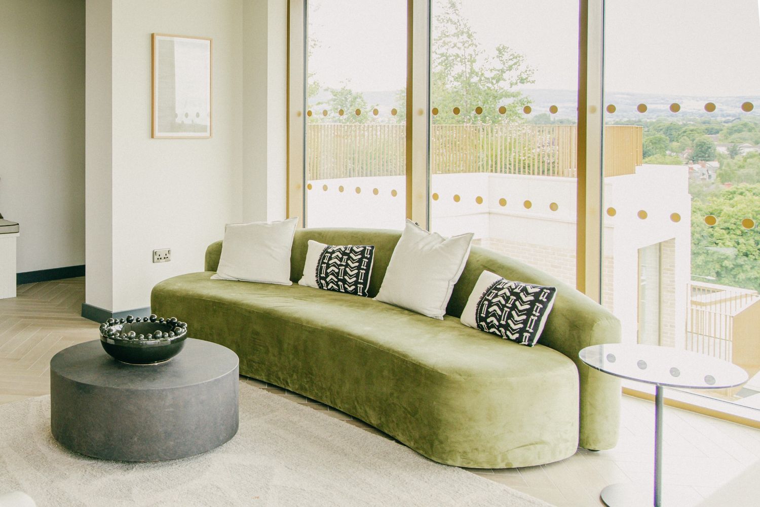 Bright living room with a green velvet sofa, black round coffee table, and natural light streaming through large windows in Dublin apartment