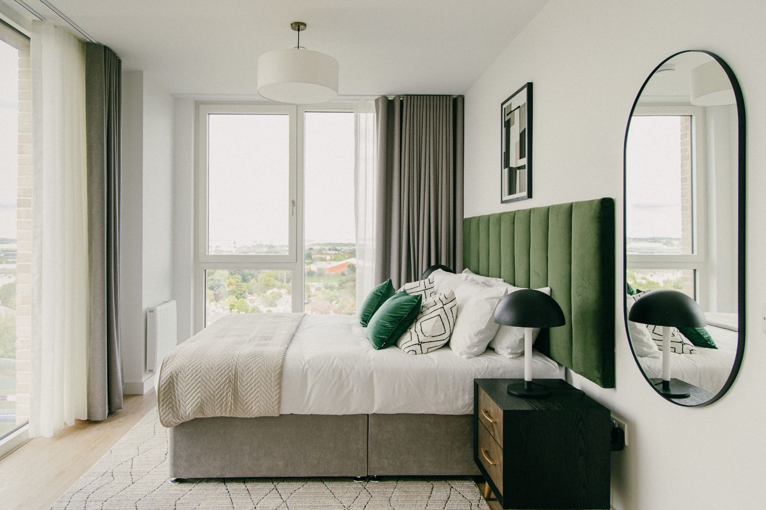 Airy and modern bedroom with a green velvet headboard and floor-to-ceiling windows, captured in soft daylight.