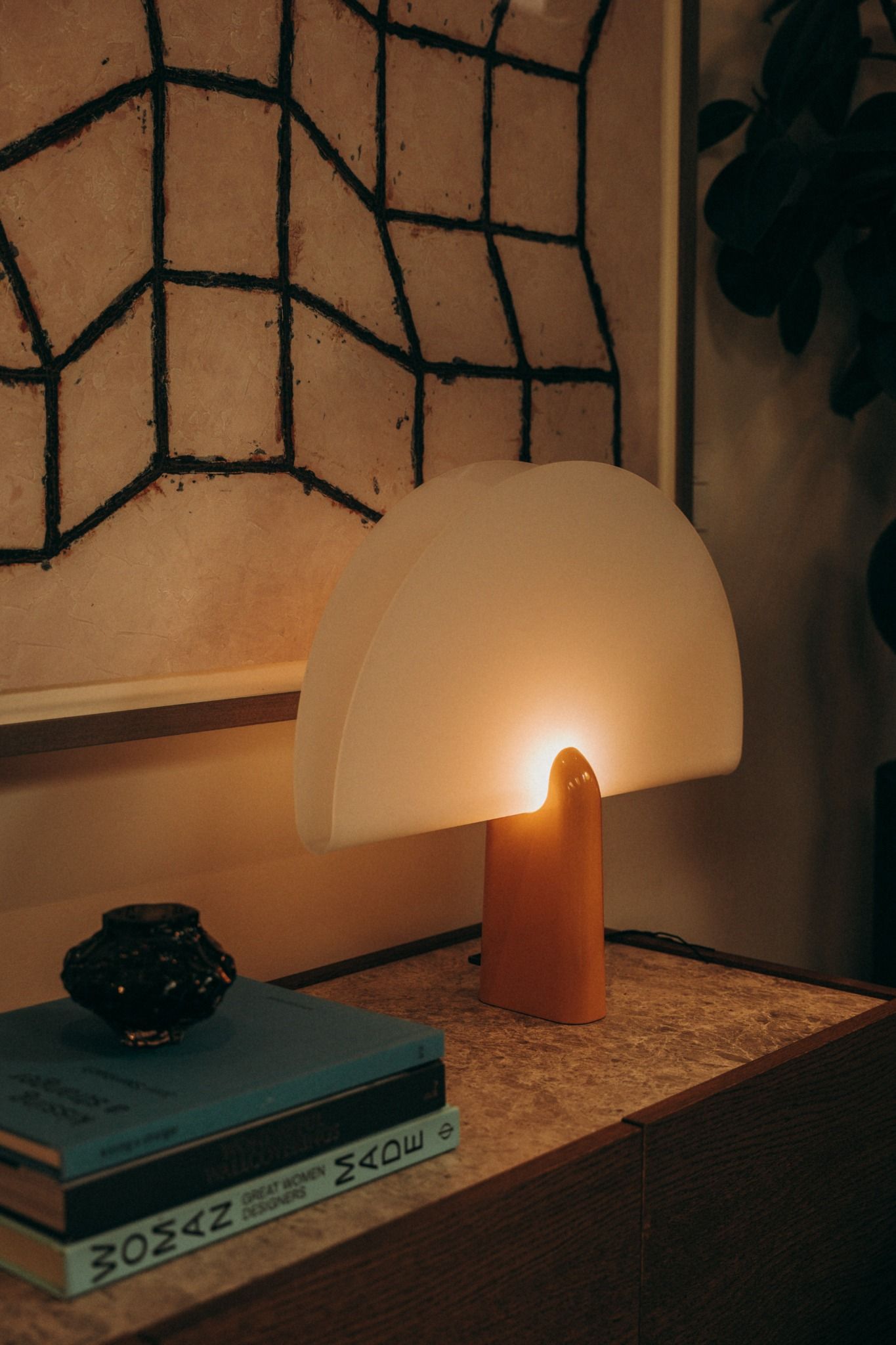 Mid-century modern table lamp glowing beside a stack of design books and abstract artwork — styled interior captured by Sigi Photography in