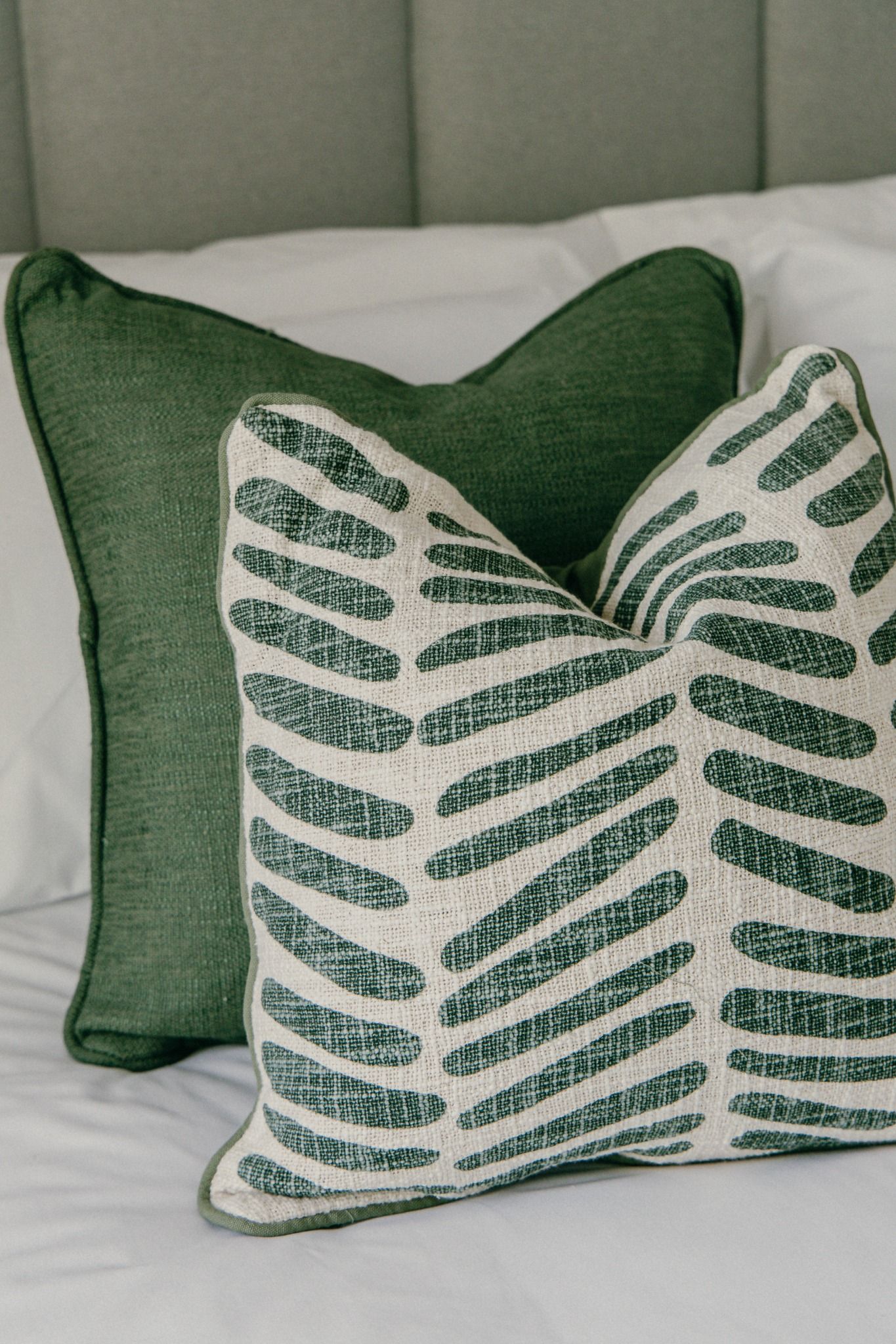 Close-up detail of layered green cushions on a white bed — simple, soft interior styling captured in natural light in Dublin.
