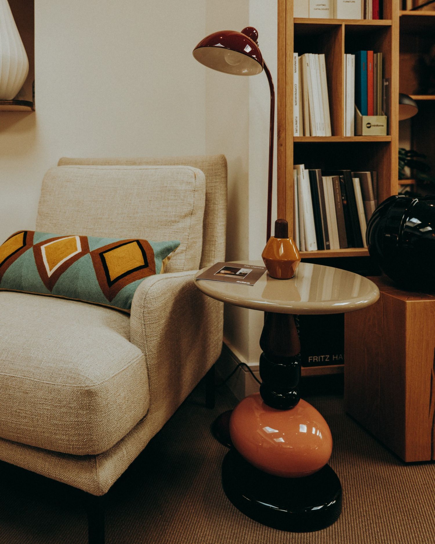 Mid-century armchair with graphic cushion and sculptural side table beside a red lamp — interior by Sigi in Dublin.