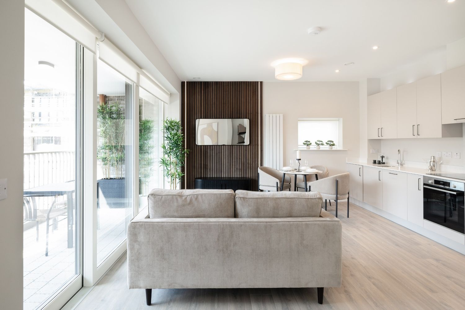 Open-plan living room and kitchen with neutral furnishings, wood accents, and large glass doors in Dublin home