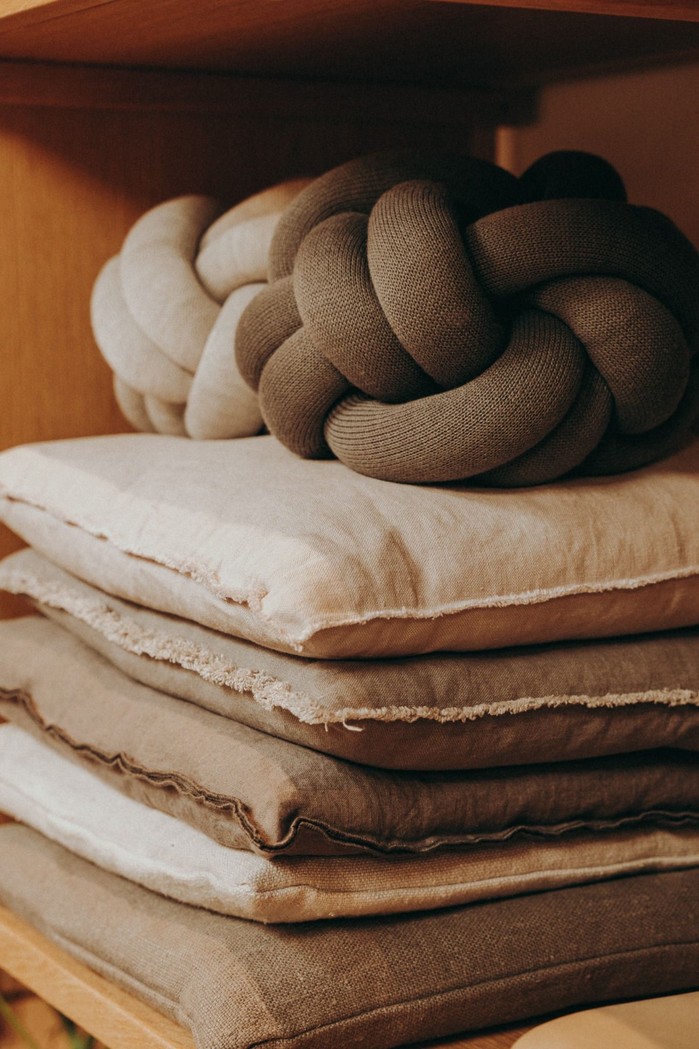 Soft stack of neutral-toned linen pillows and chunky knitted knot cushions on wooden shelves-Nordic-inspired textures photographed in Dublin