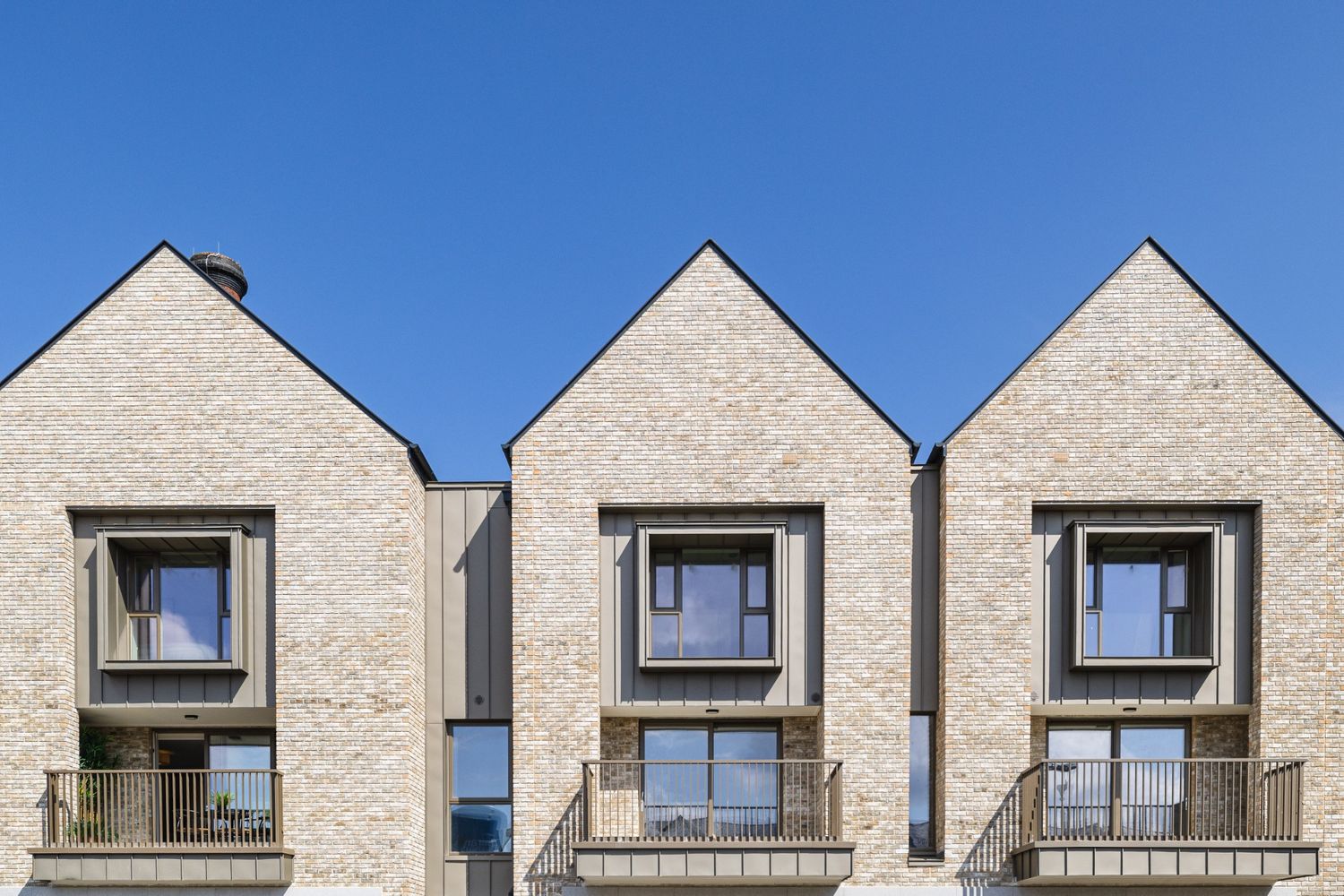 Contemporary brick townhouses with geometric windows and balconies under a clear blue sky in Dublin.