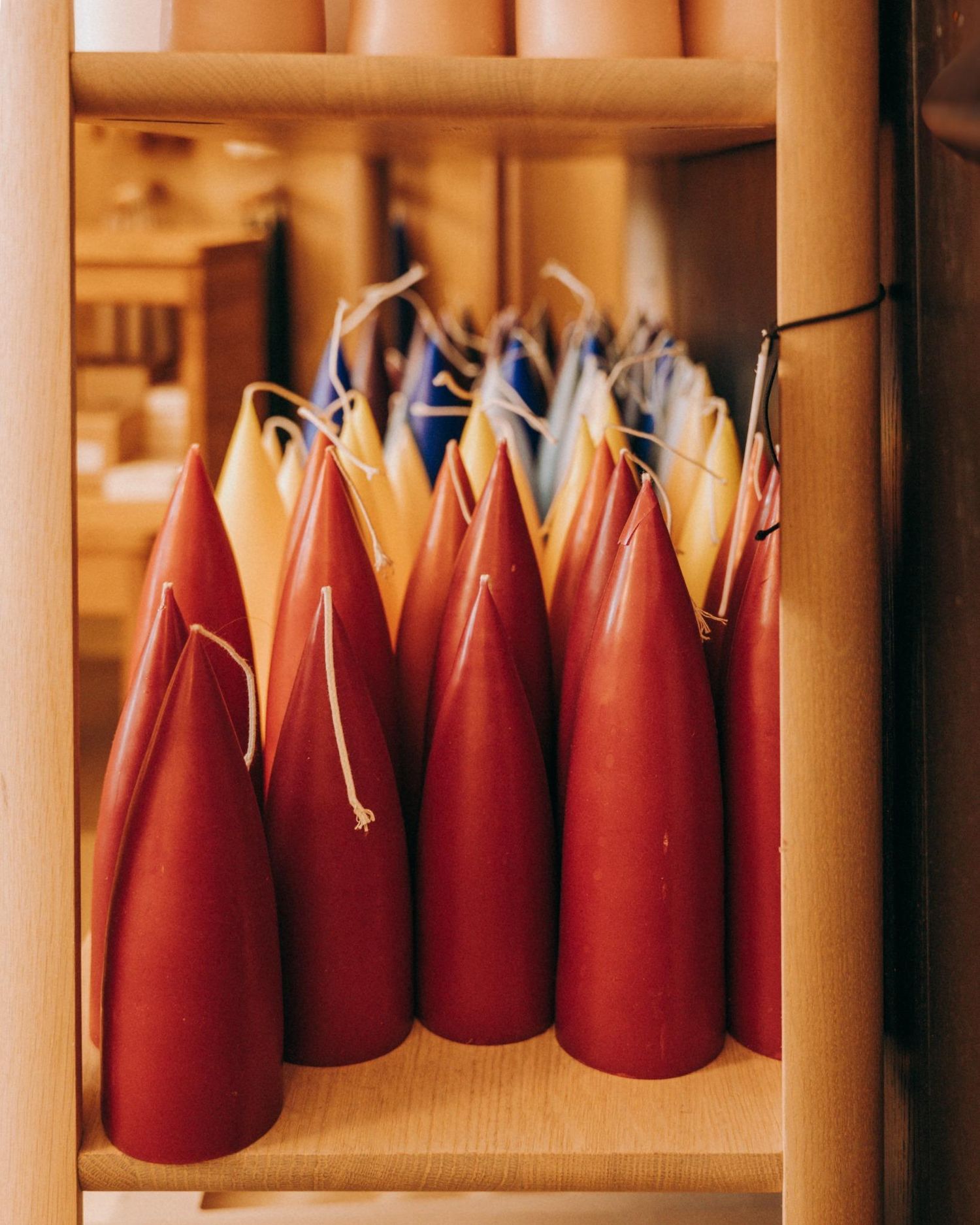 Handcrafted taper candles in rich reds and yellows, neatly arranged on natural wood shelving in a Nordic-inspired Dublin interior shop.