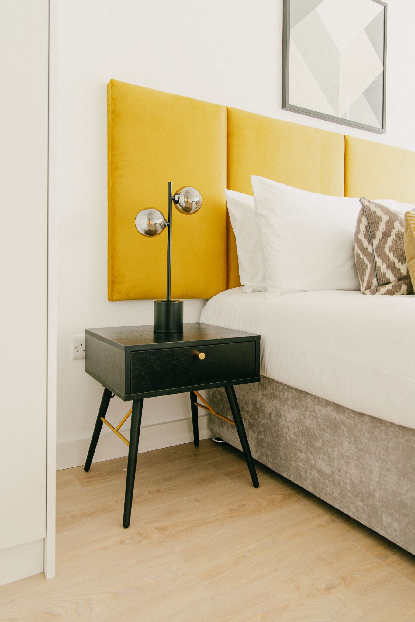 Detail of yellow upholstered headboard with black bedside table and chrome lamp, photographed in a stylish Dublin bedroom.