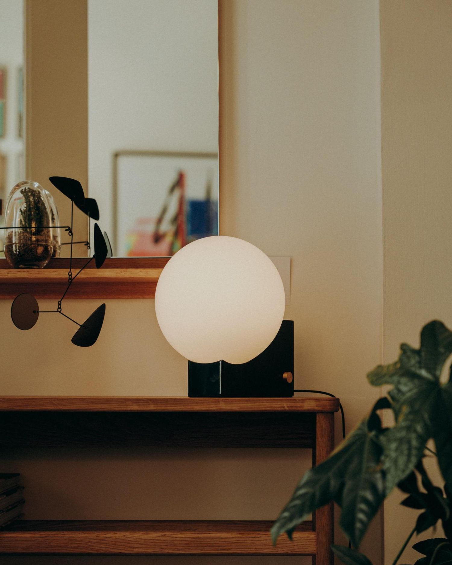 Minimalist round orb lamp placed on a wooden floating shelf with sculptural mobile and greenery — styled Nordic home detail photographed in