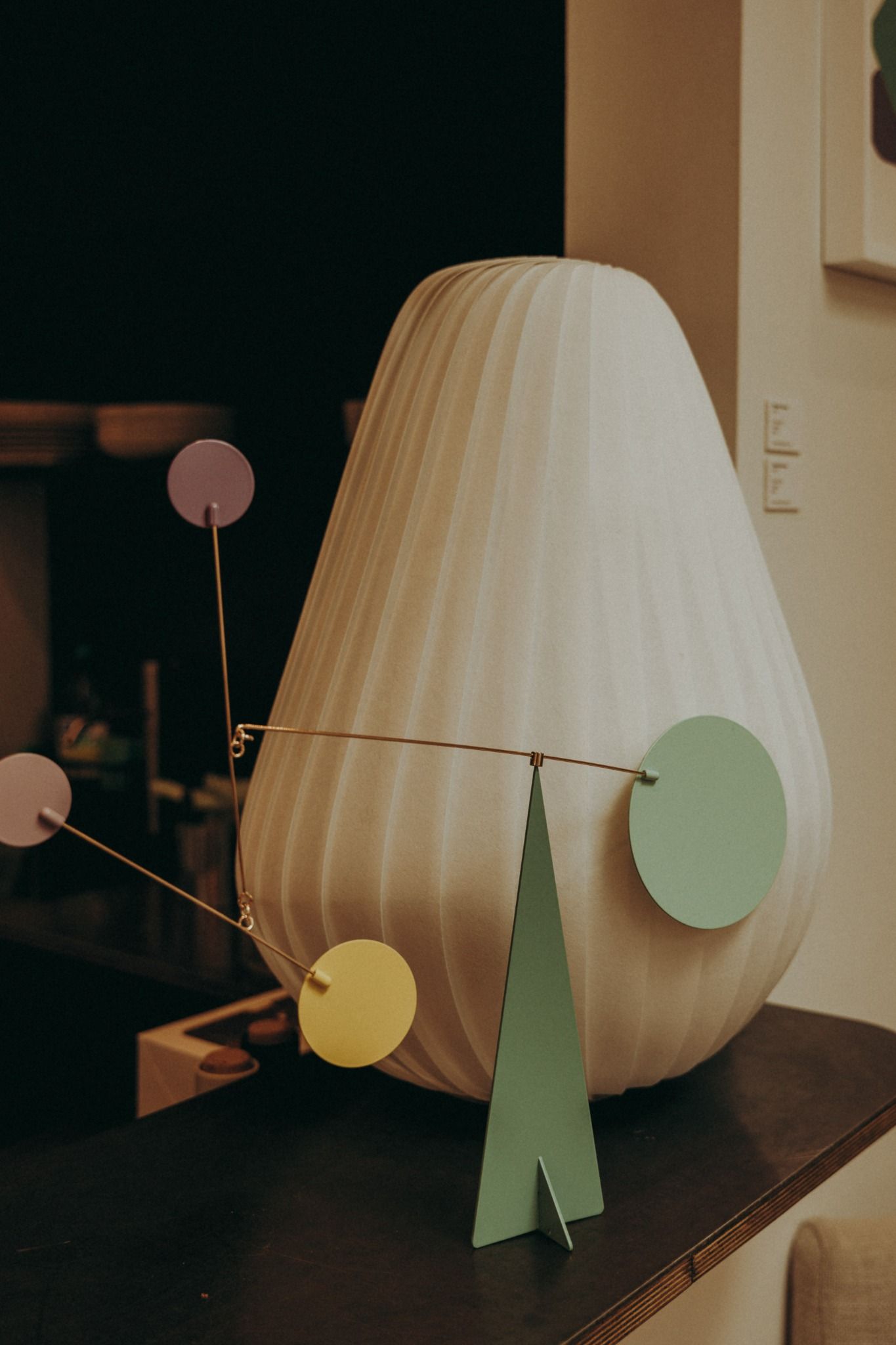Nordic-style sculptural lamp with colourful mobile detail on dark wood surface — playful and modern vignette photographed by Sigi in Dublin.