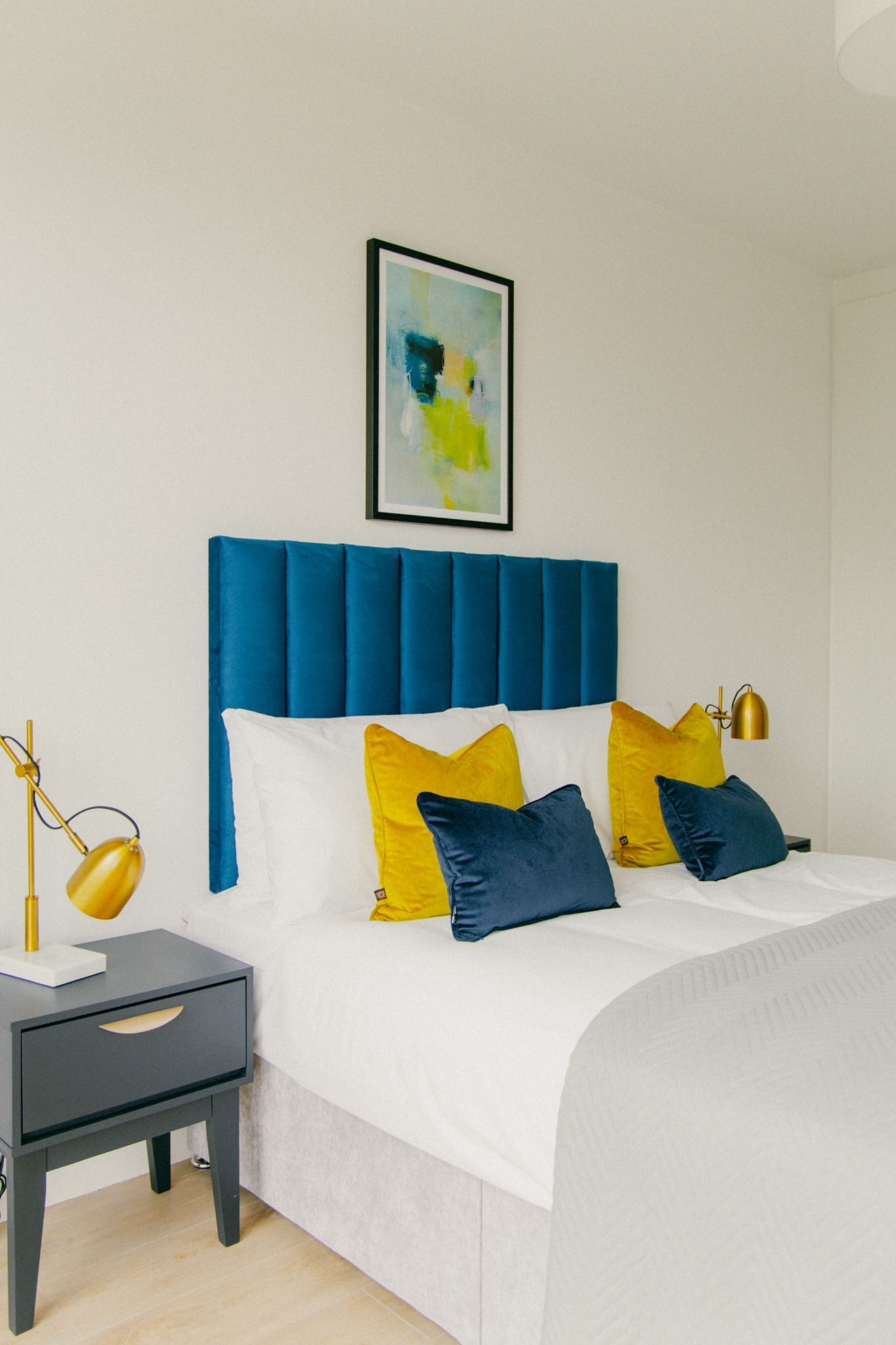 Close-up of bed styling with mustard yellow and navy pillows against a deep blue velvet headboard in a Dublin home.