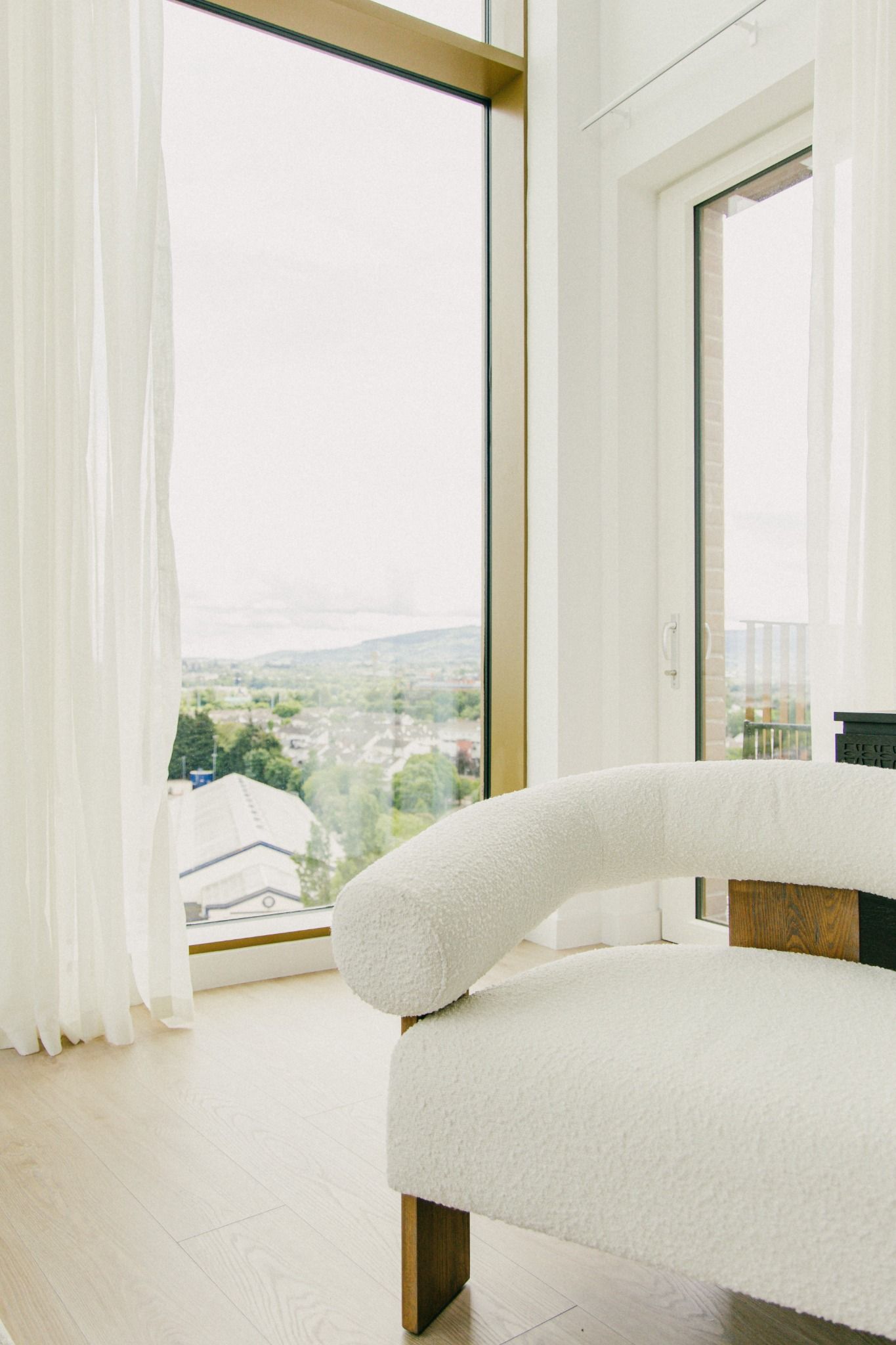 Bright corner view featuring a boucle white armchair, soft curtains, and a panoramic cityscape outside — Dublin property interior.