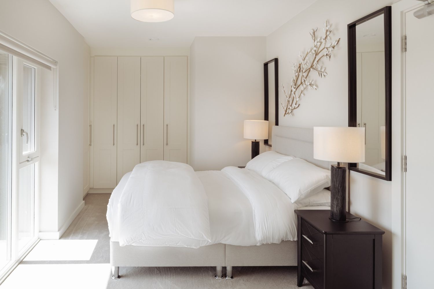 Airy minimalist bedroom with white walls, double bed, built-in wardrobes, and natural daylight in Dublin.