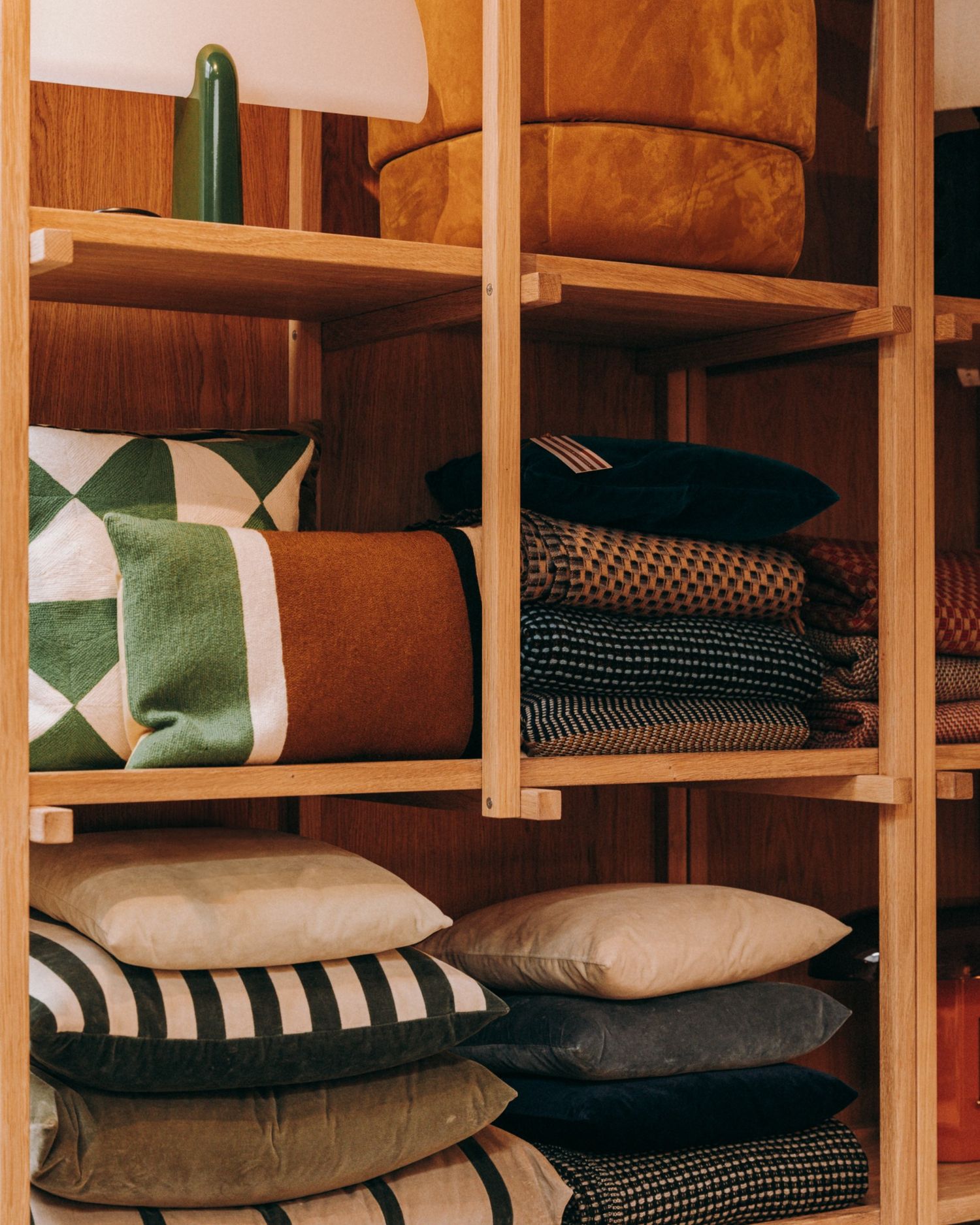 Earth-toned and patterned cushions neatly arranged on open wooden shelves — natural texture-focused interior image by Sigi Photography.