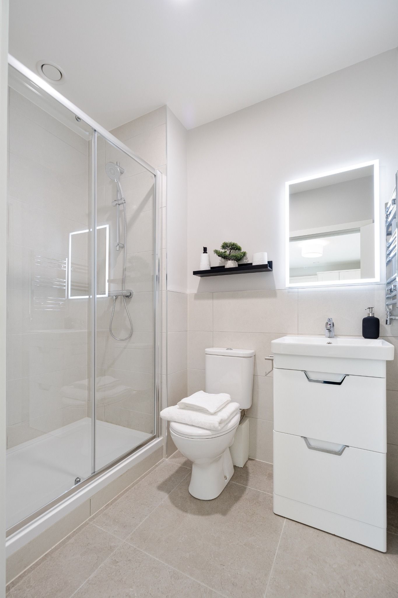 Modern white-tiled bathroom with glass shower and LED mirror, softly lit by natural light in a Dublin apartment
