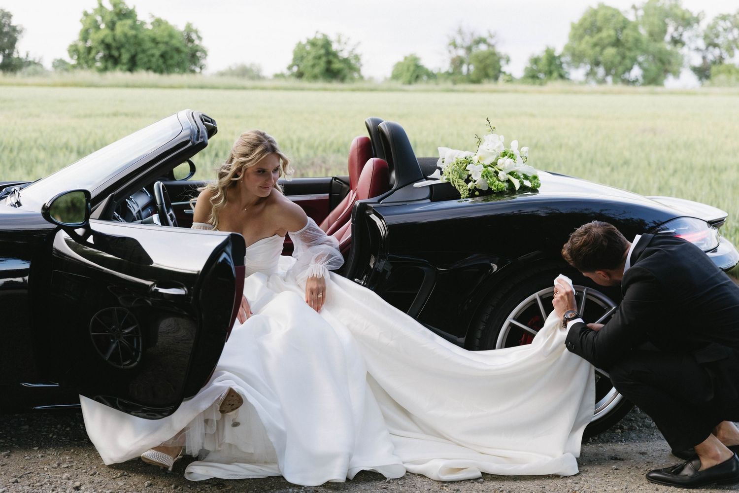 Wedding couple getting into a black convertible car with flowing white dress.