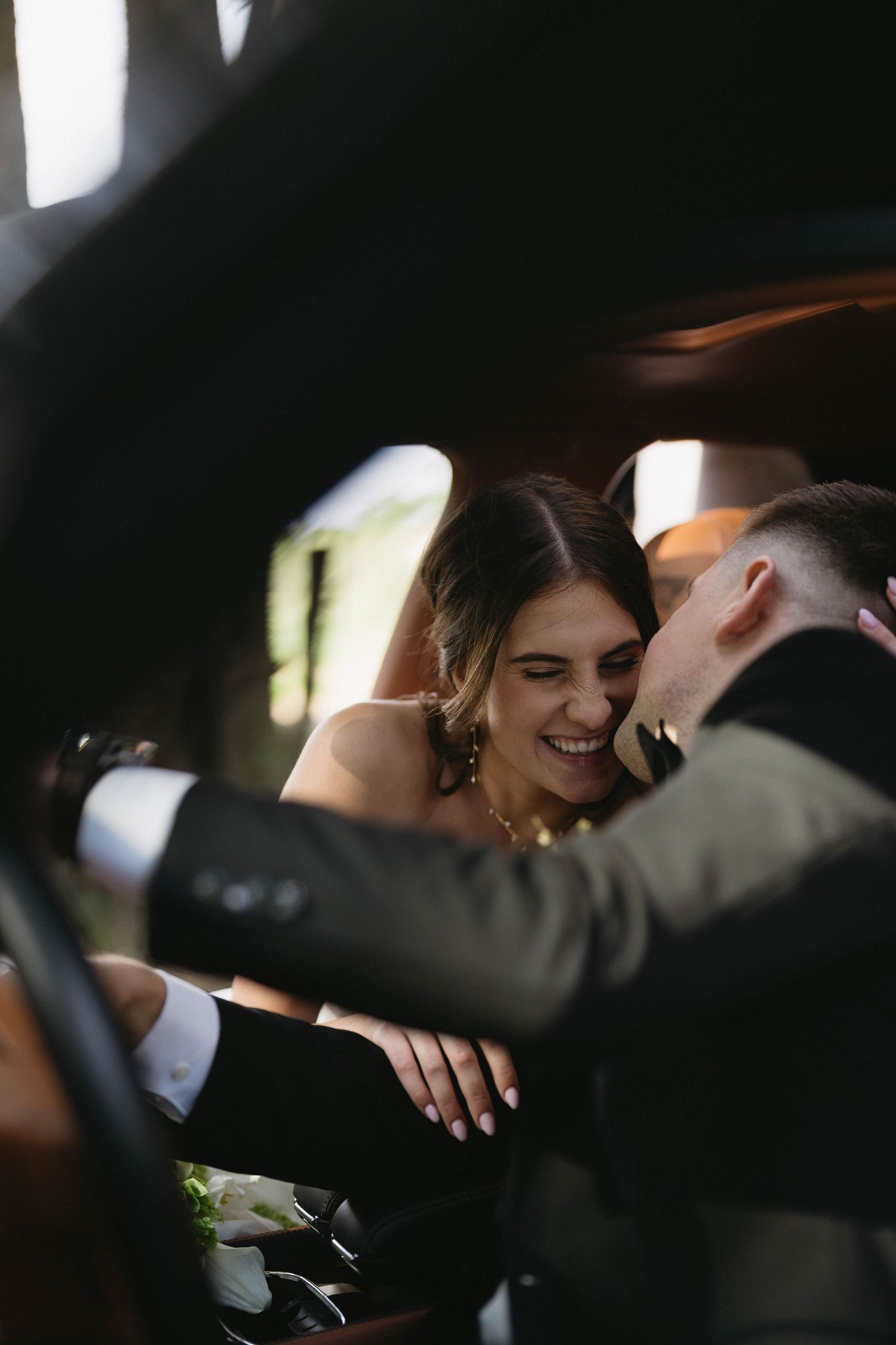 Candid moment of couple laughing together inside a vehicle on their wedding day.