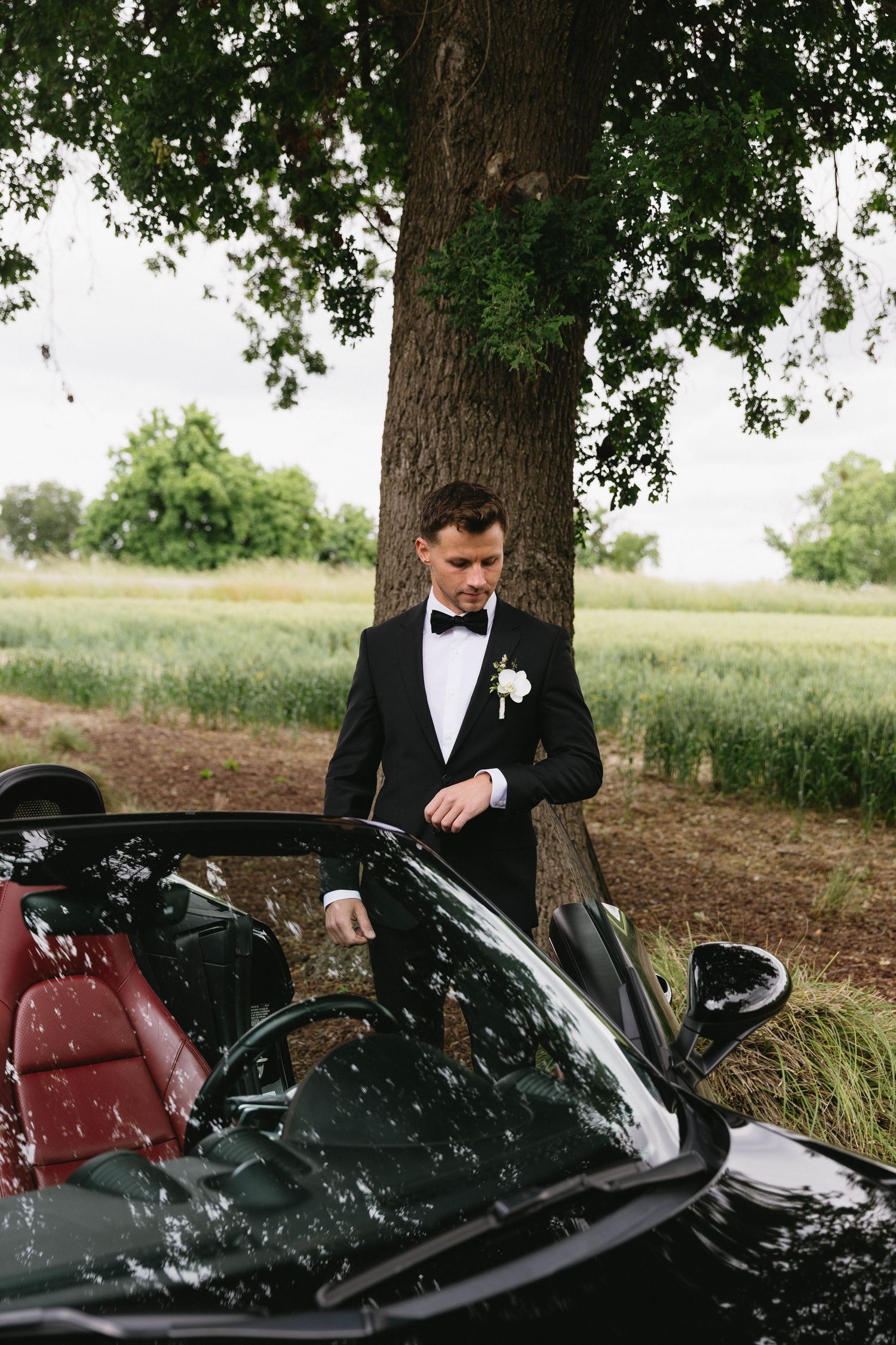 Wedding photography featuring black luxury sports car and formal attire in natural setting.