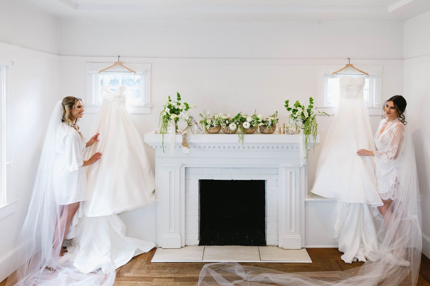 White wedding dresses displayed on either side of a decorative fireplace with green floral accents.