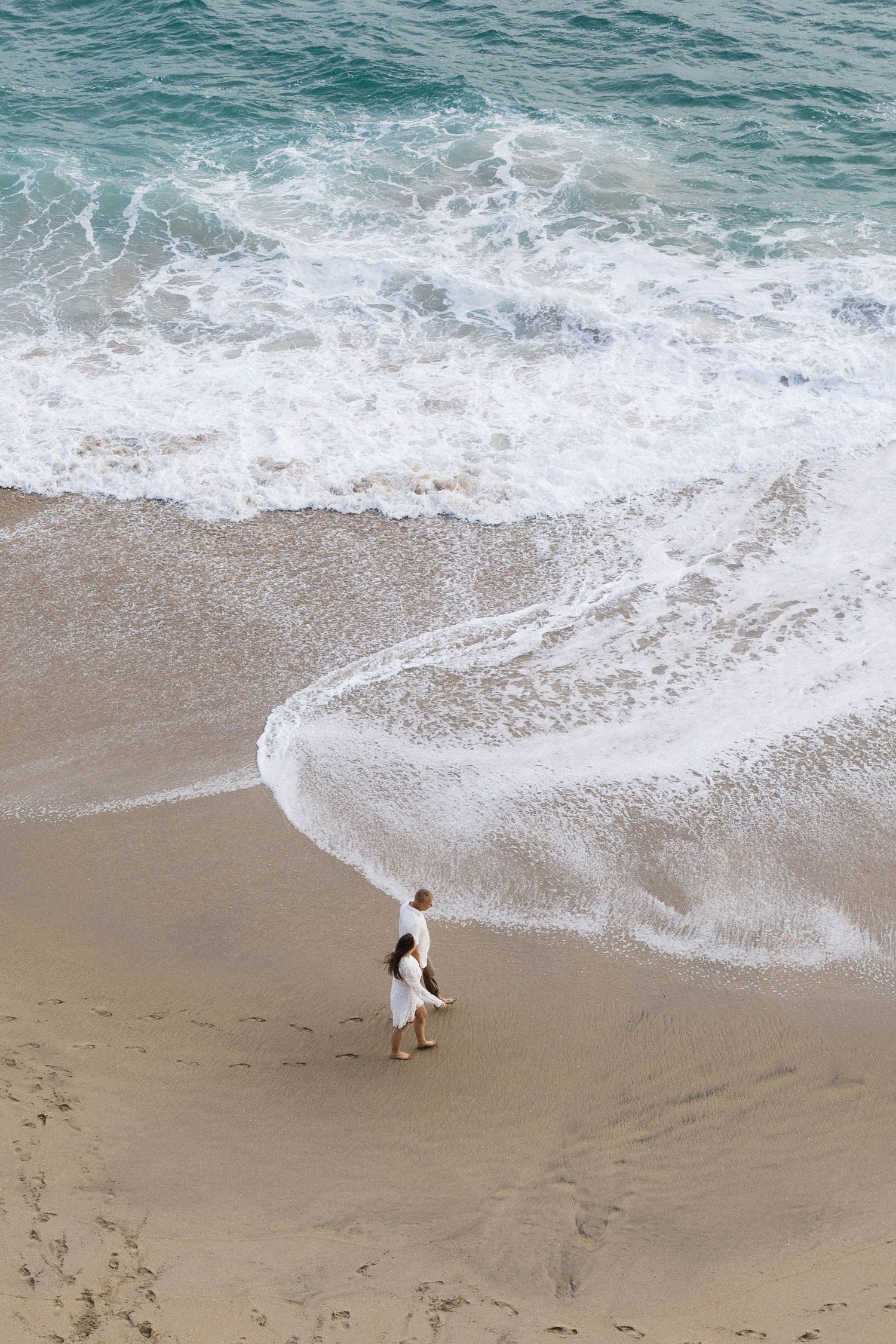 A seagull walks along the sandy beach as gentle waves roll onto the shore with turquoise ocean waters in the background.