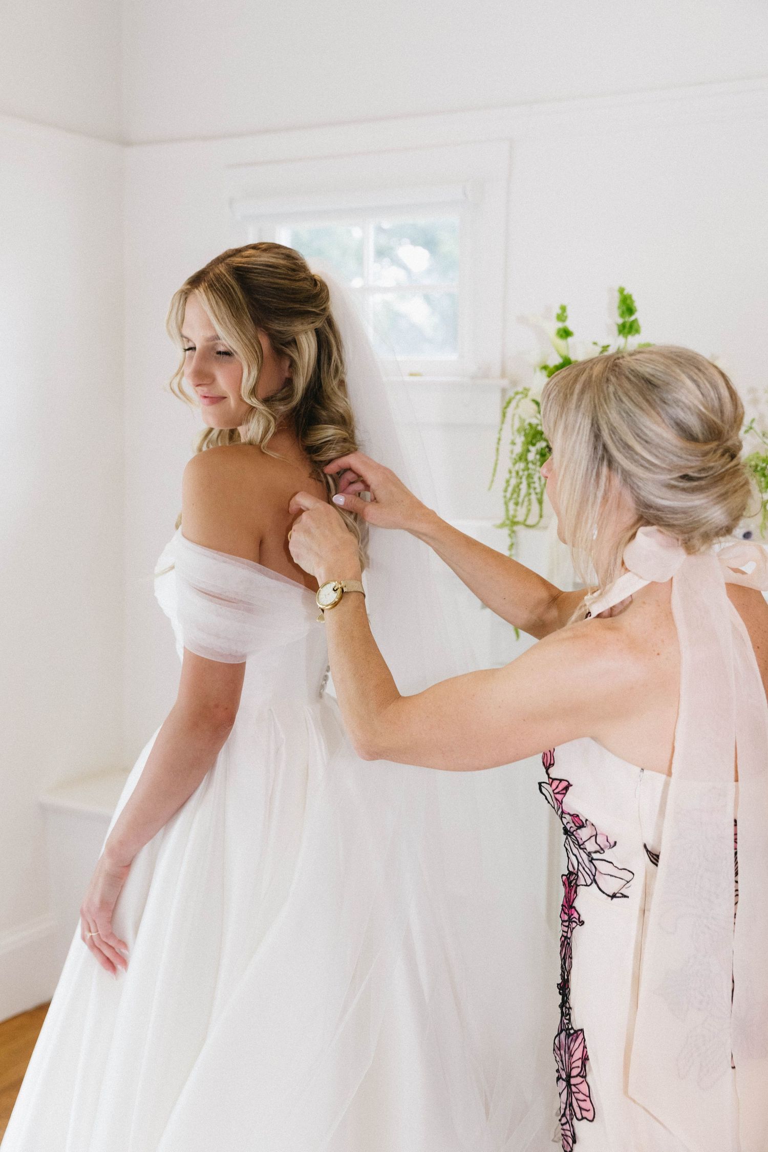 Wedding dress preparation with flowing train in sunlit white room.