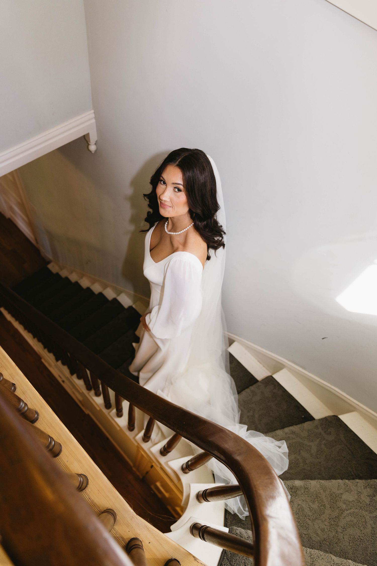 A bride in a white dress descends a carpeted staircase in elegant wedding day photos.