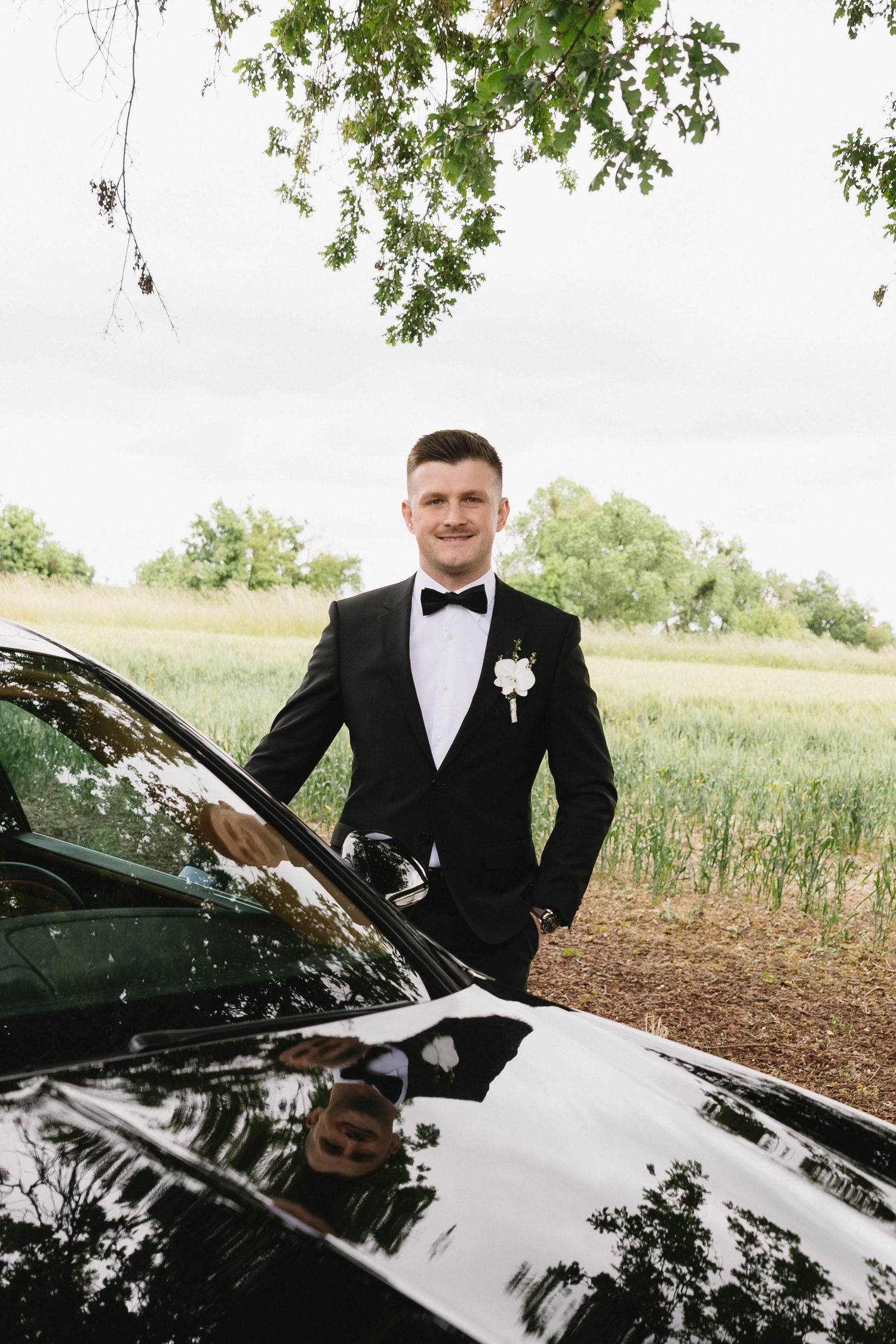 A black luxury convertible car parked outdoors with someone in formal attire standing beside it.
