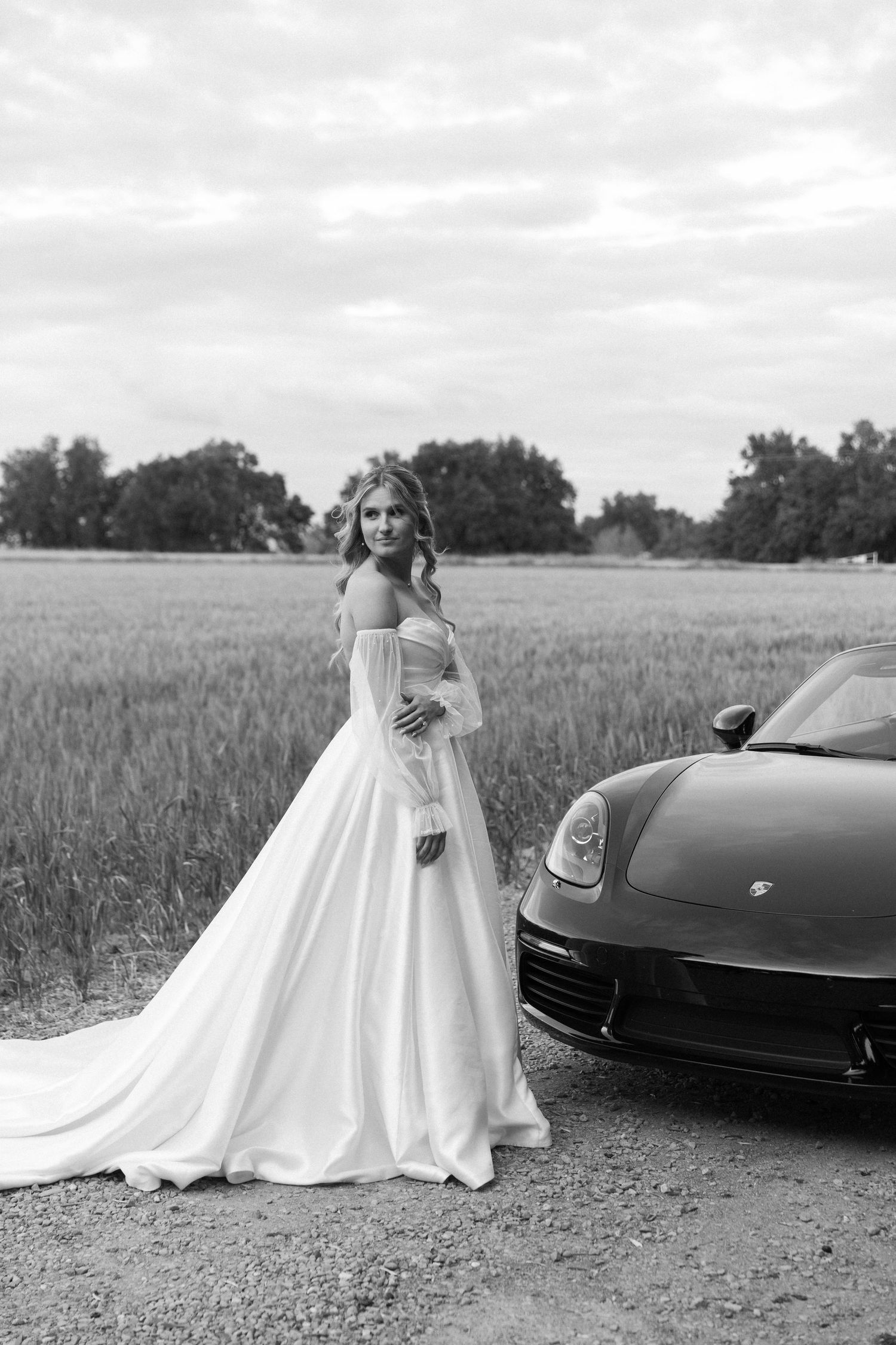 Black and white wedding photos with couple posing by sleek sports car in rural setting.