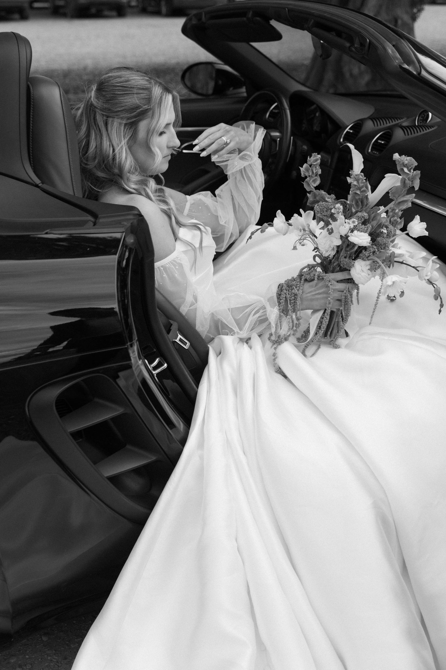 Black and white series of bride sitting in luxury car interior with floral decorations.