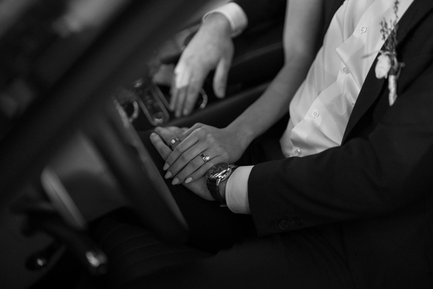Black and white close-up of clasped hands showing wedding rings and formal attire.
