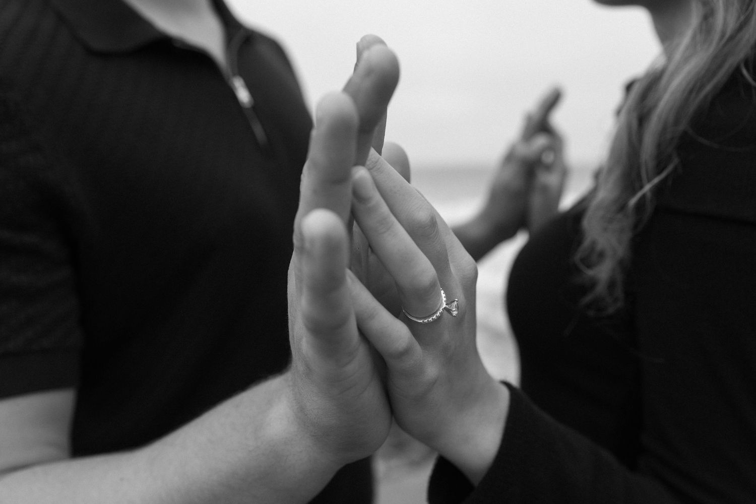 Black and white close-up of two hands clasped together with a wedding ring visible.