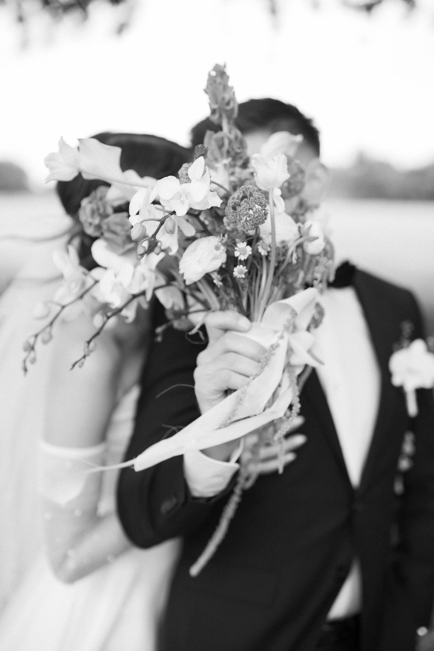 Black and white wedding photo showing couple behind a romantic floral bouquet.