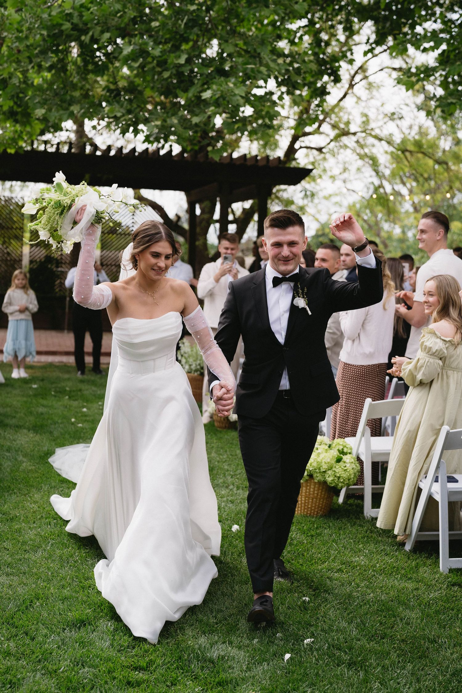 Wedding celebration with dancing couples on a green lawn surrounded by white chairs.