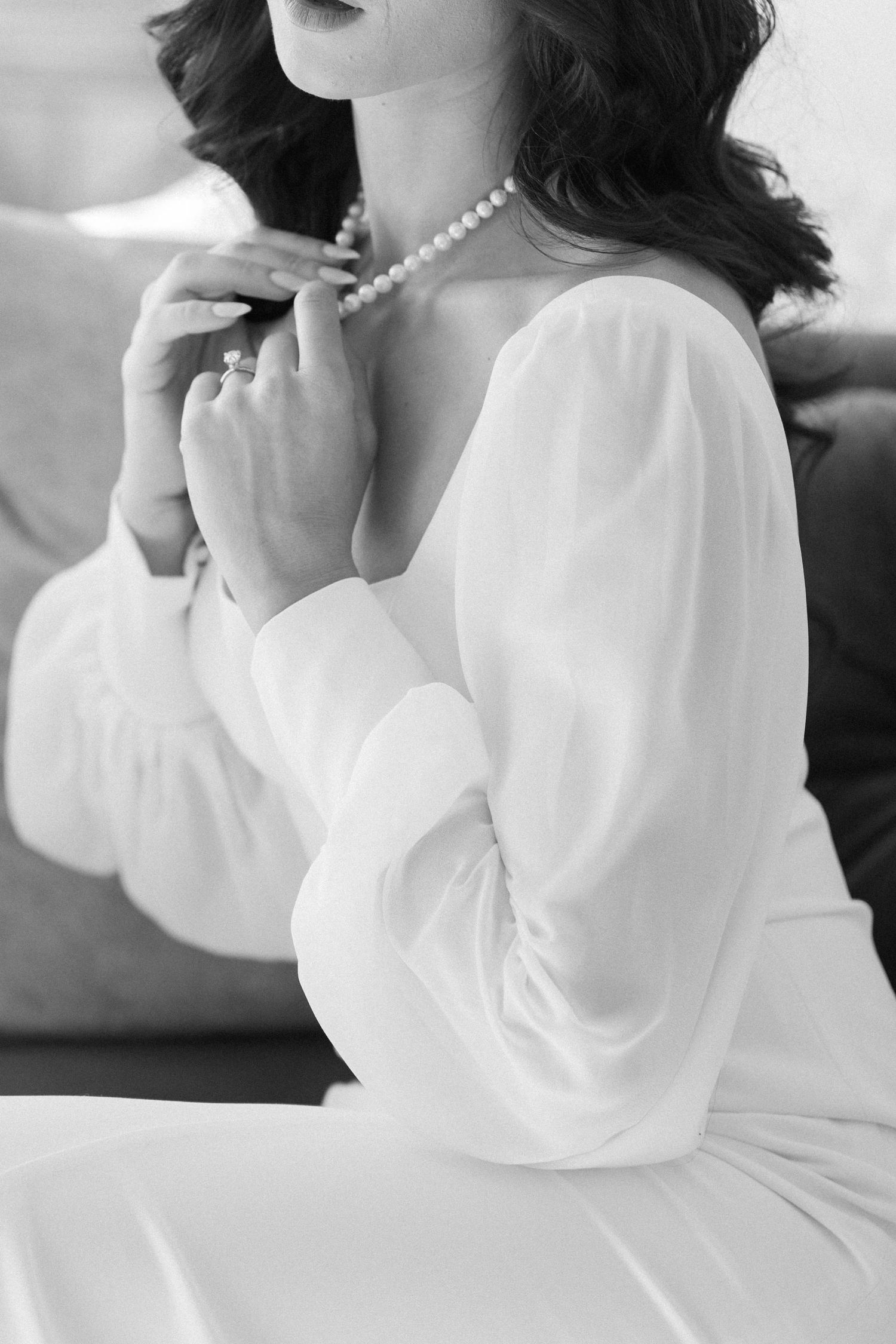 Elegant black and white portrait showing a pearl necklace and flowing white dress with long sleeves.