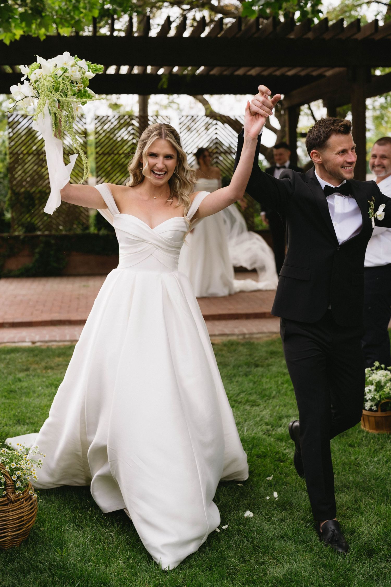 Couple celebrating their wedding with energetic dance moves on a grass lawn.