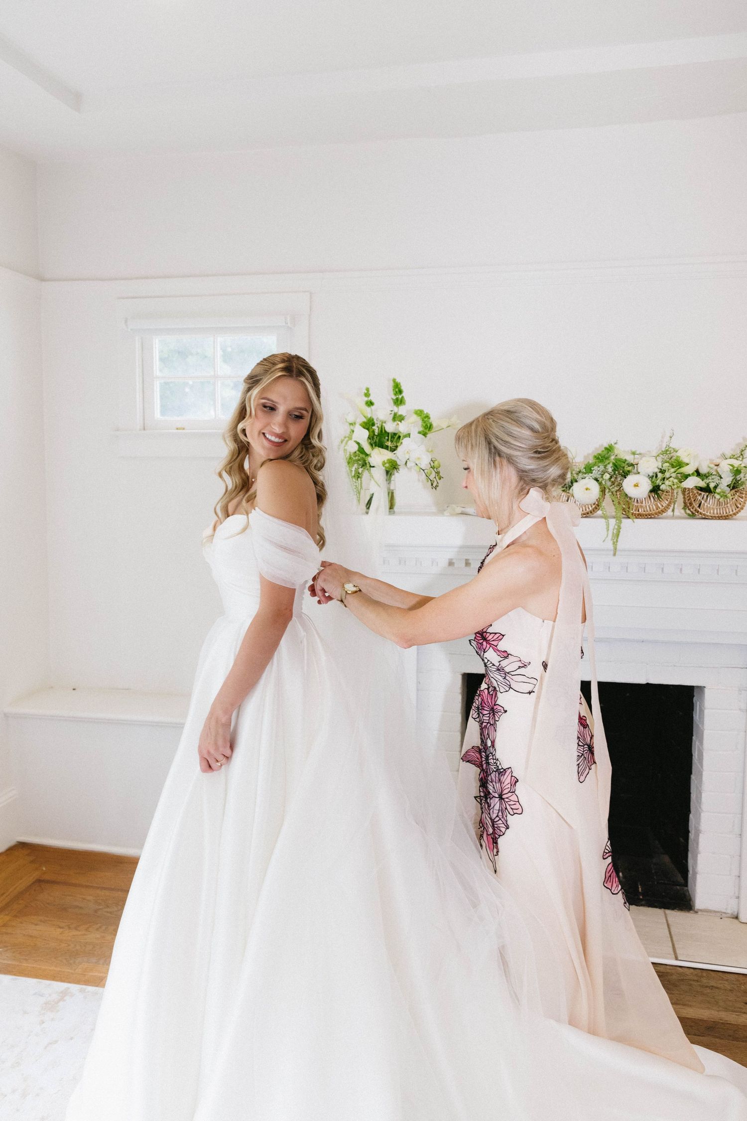 Final wedding dress fitting in bright white room with decorative fireplace.