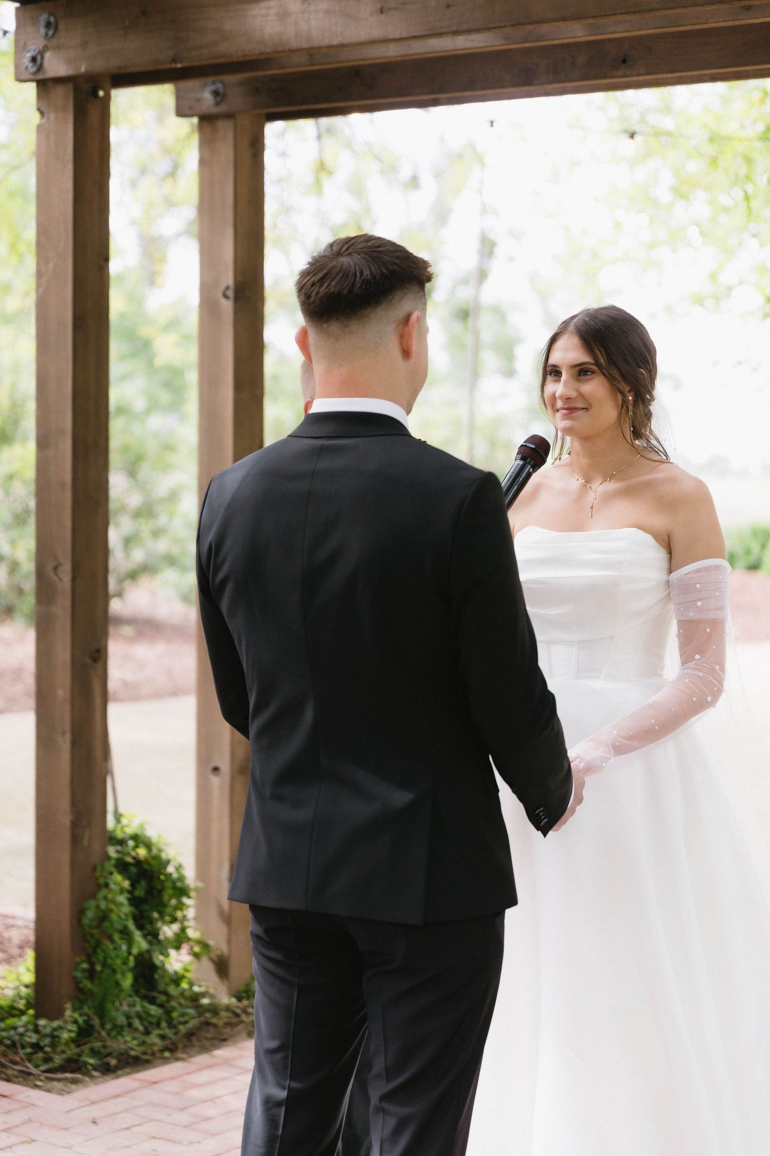 An intimate wedding ceremony moment captured under a wooden pergola with natural lighting.