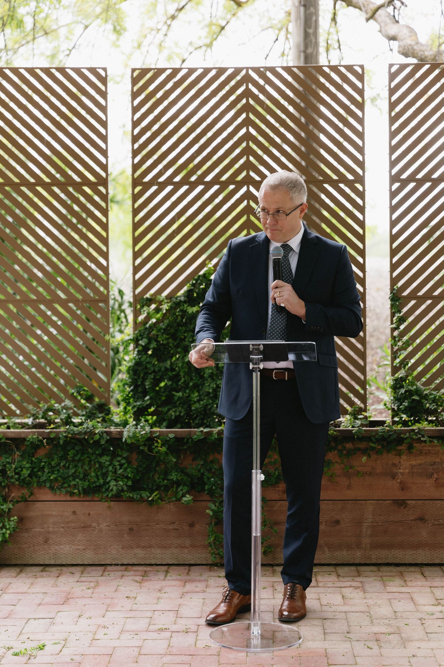 A wedding ceremony setup with geometric wooden screens and a modern clear podium in an outdoor garden setting.