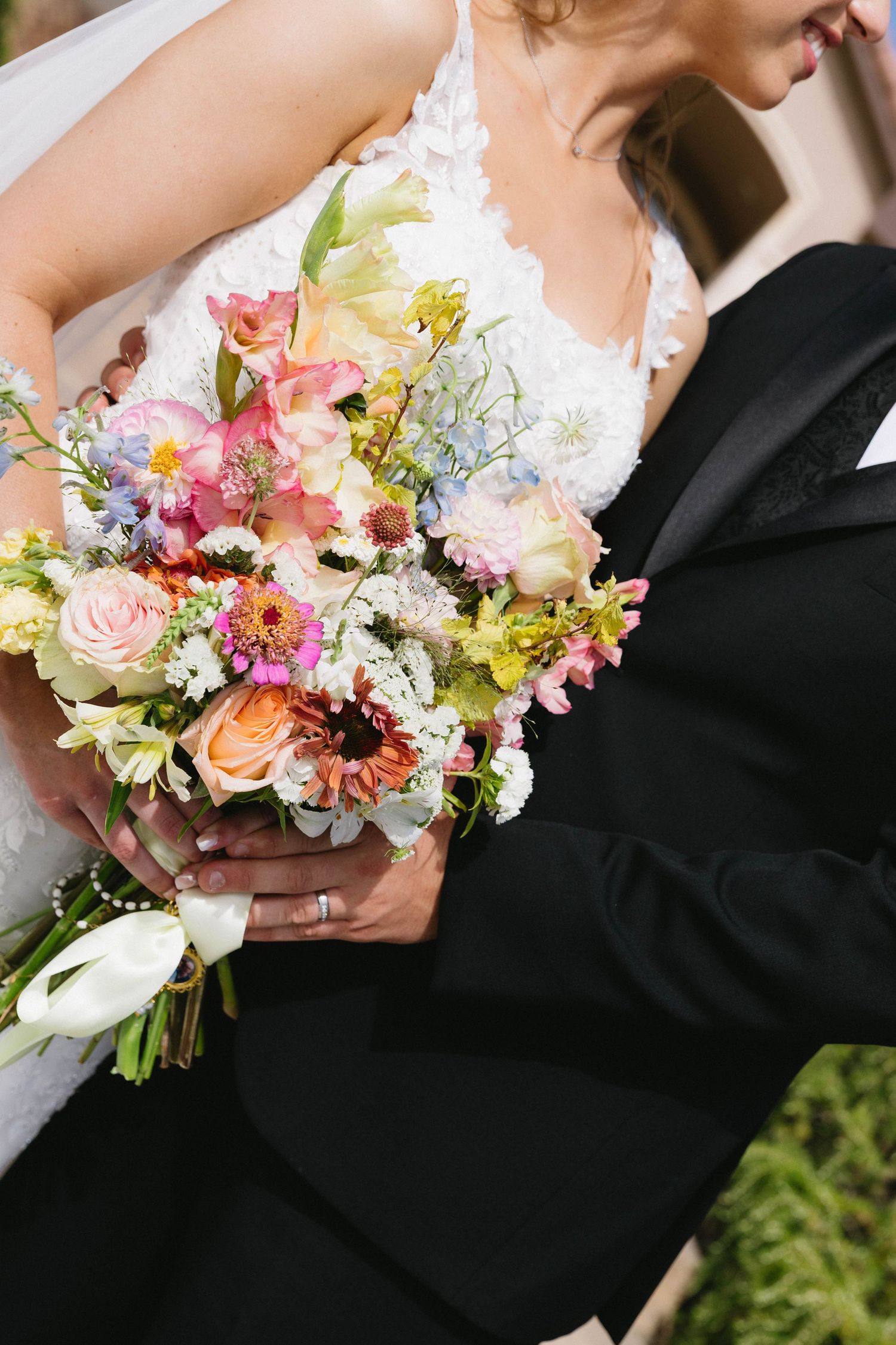 Colorful spring wedding bouquet with roses, daisies and mixed flowers held between two people.