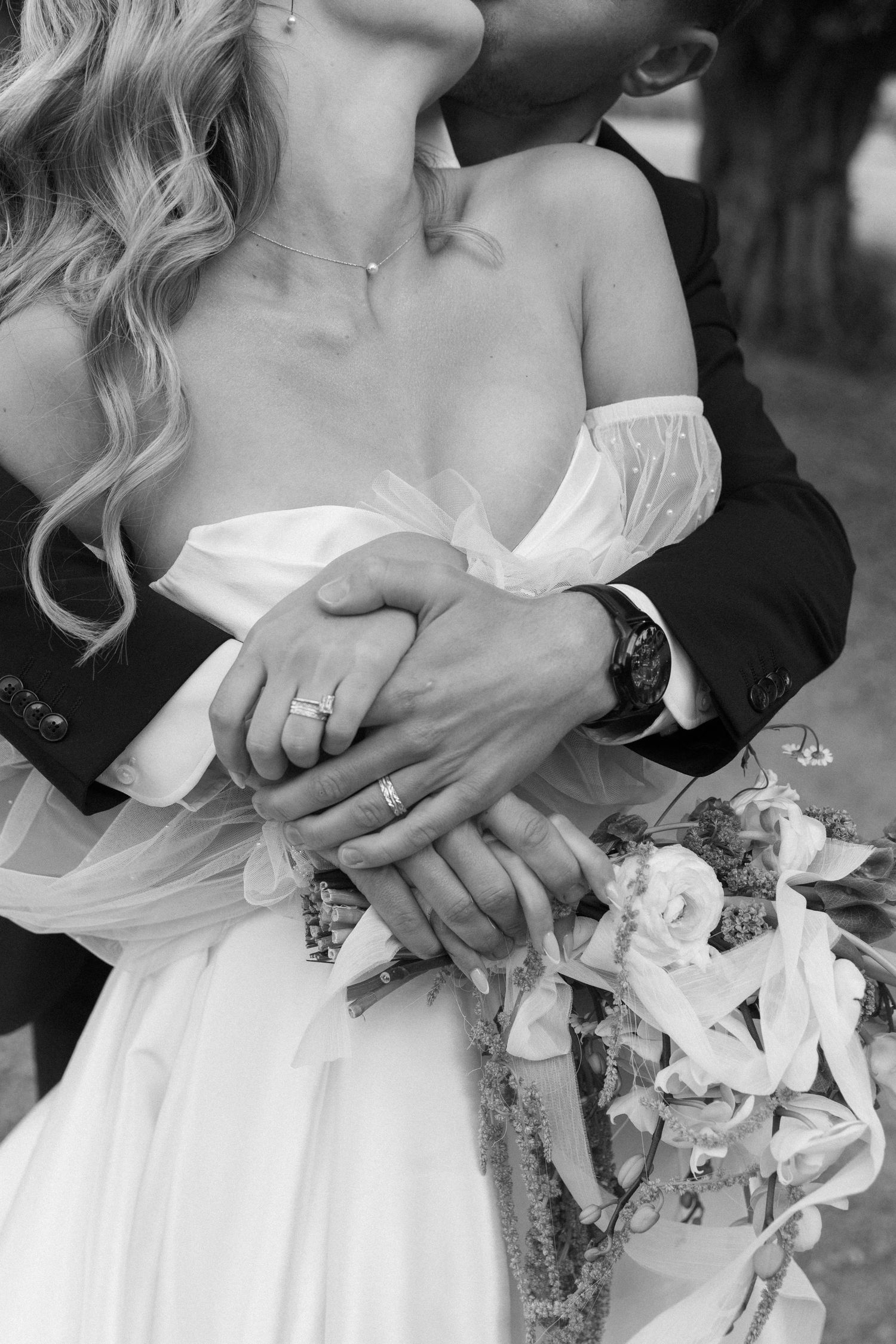 Close-up black and white wedding photo showing hands holding a bouquet against a white dress.