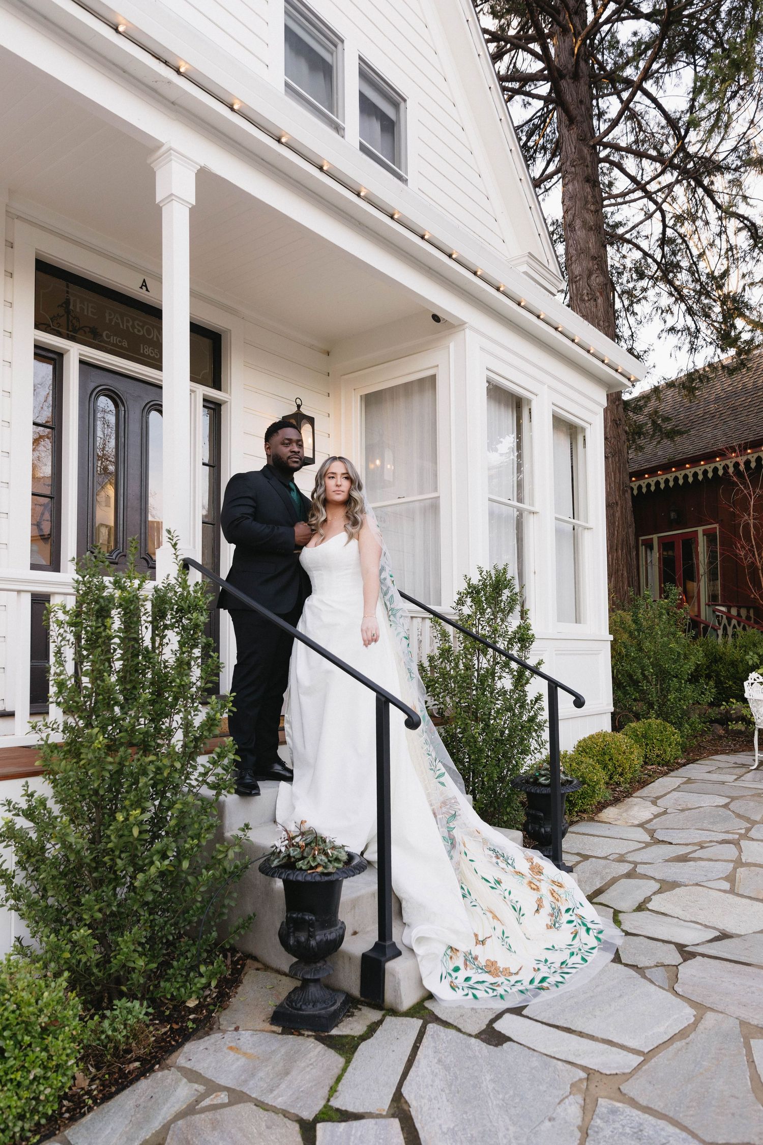 A romantic wedding couple shares a playful dance moment on a stone patio outside a white columned building.