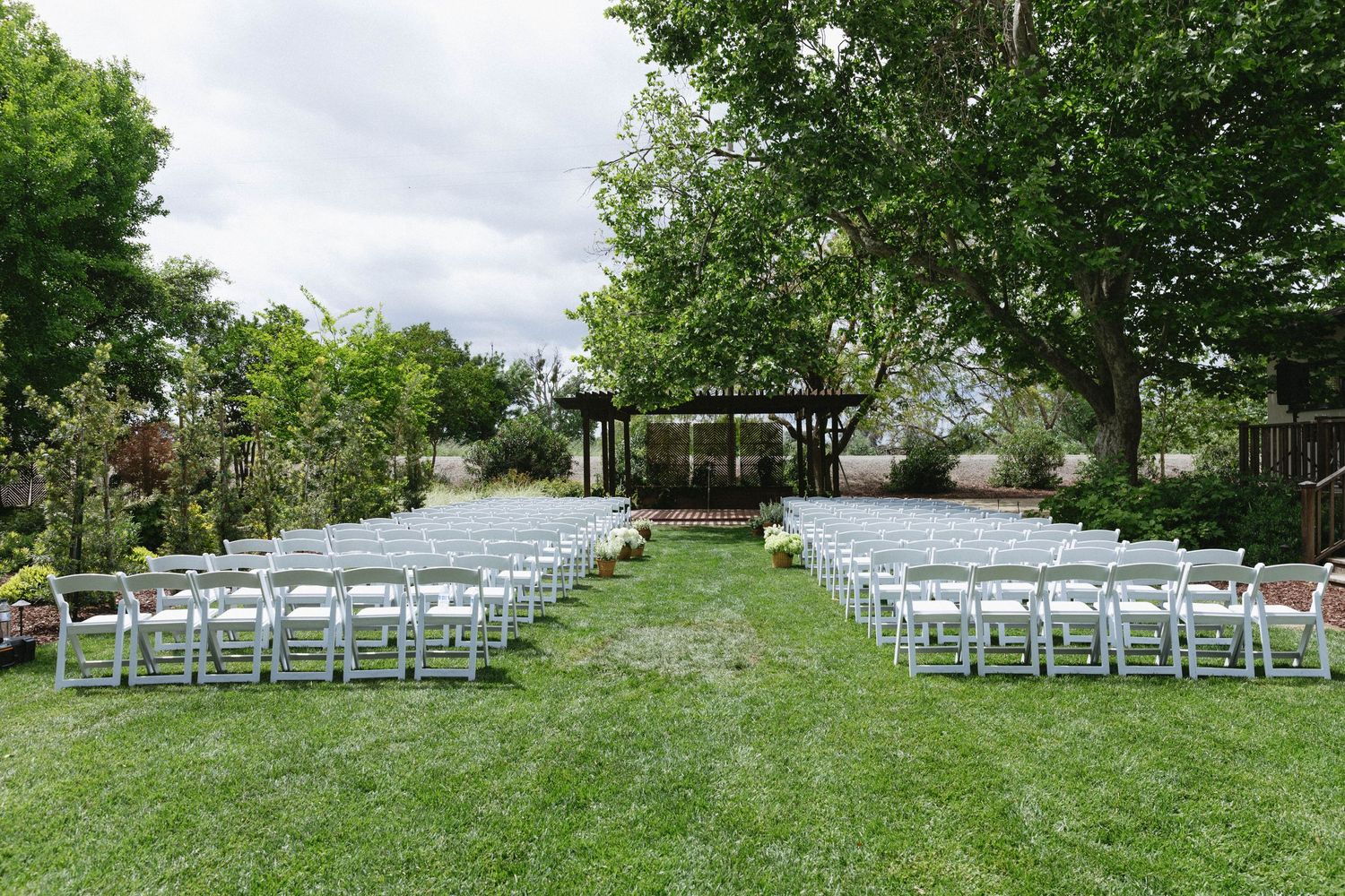 White chairs arranged in rows for an outdoor wedding ceremony under trees.
