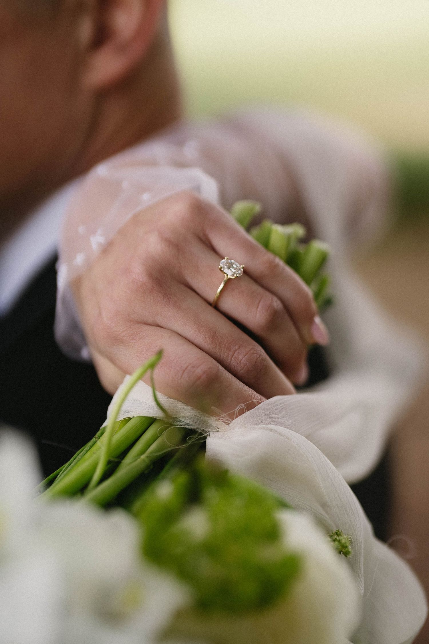Close-up of hands holding white flowers with an engagement ring detail.