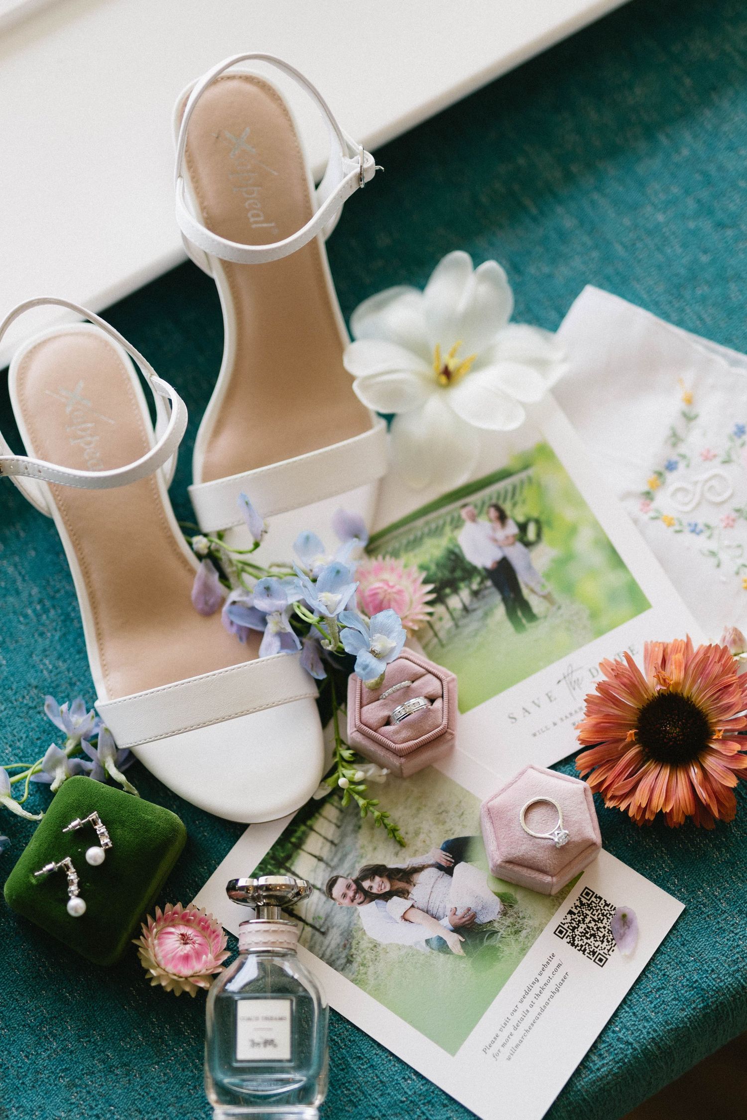 Wedding accessories including white sandals, perfume, and floral details on teal fabric.