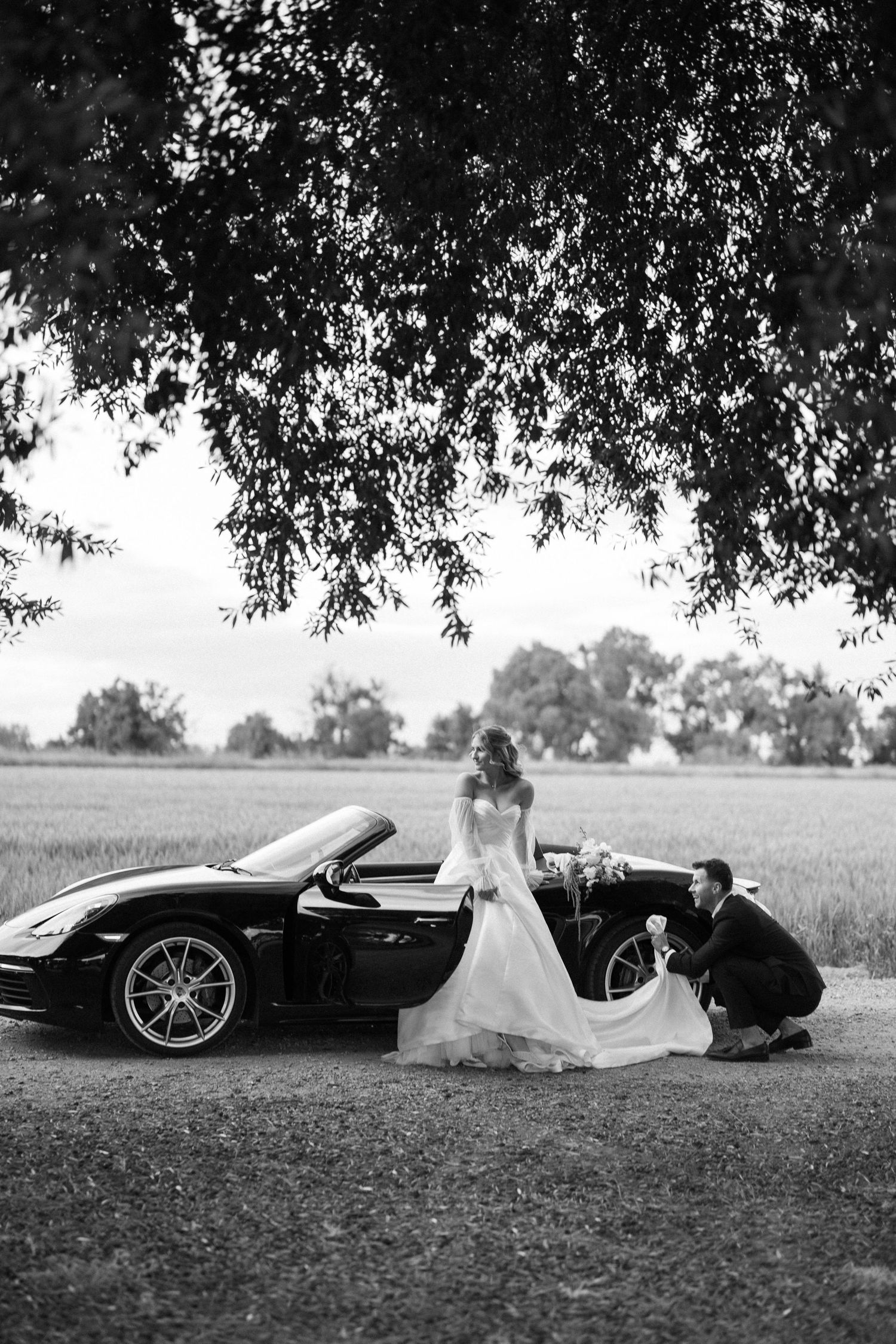 Black and white wedding photos with luxury sports car in a dramatic field setting.